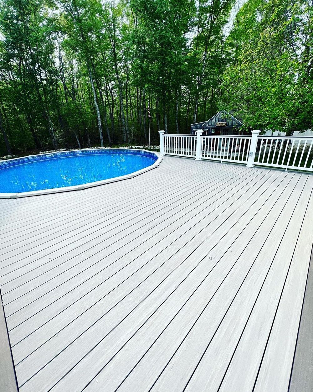 A large wooden deck with a swimming pool in the background