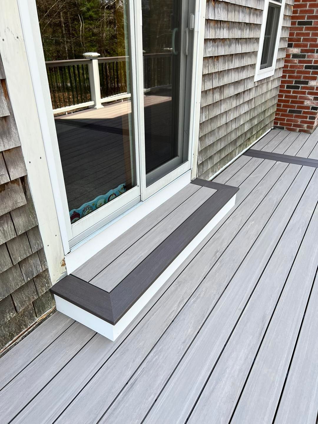 A gray deck with a bench in front of a sliding glass door