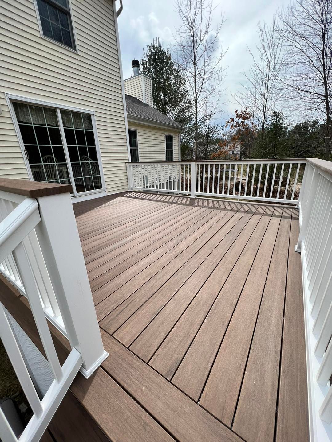 A wooden deck with a white railing and a house in the background