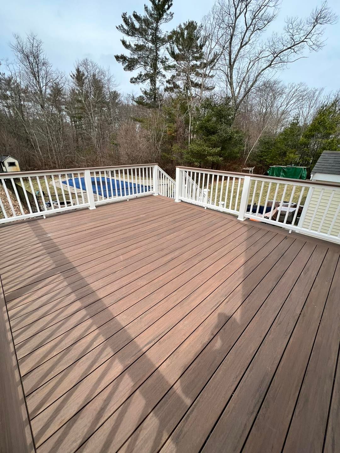 A large wooden deck with a white railing and trees in the background