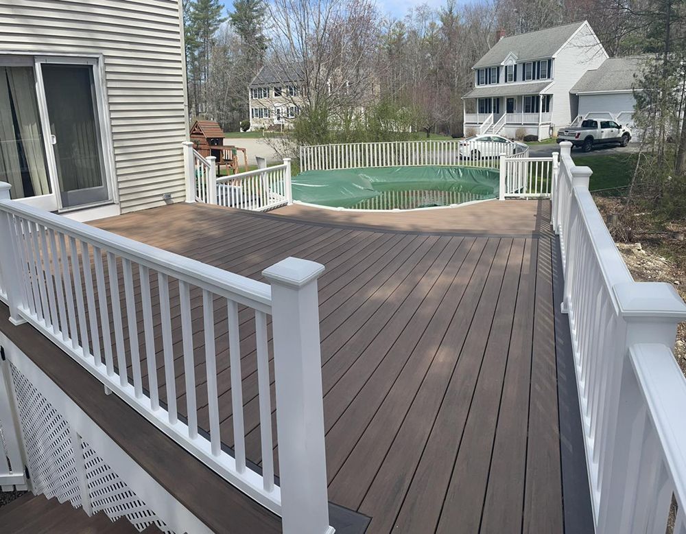 A deck with a white railing and a pool in the background