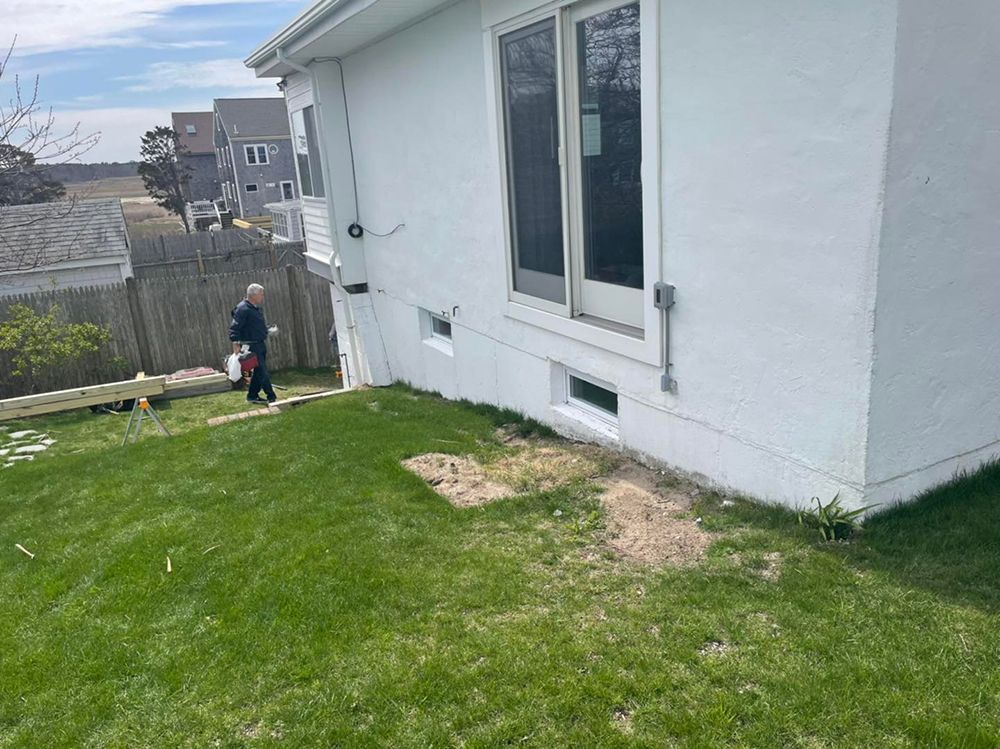 A man is standing in front of a white house in a backyard