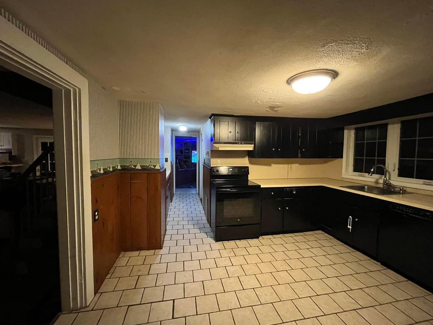 An empty kitchen with black cabinets and white tile floors
