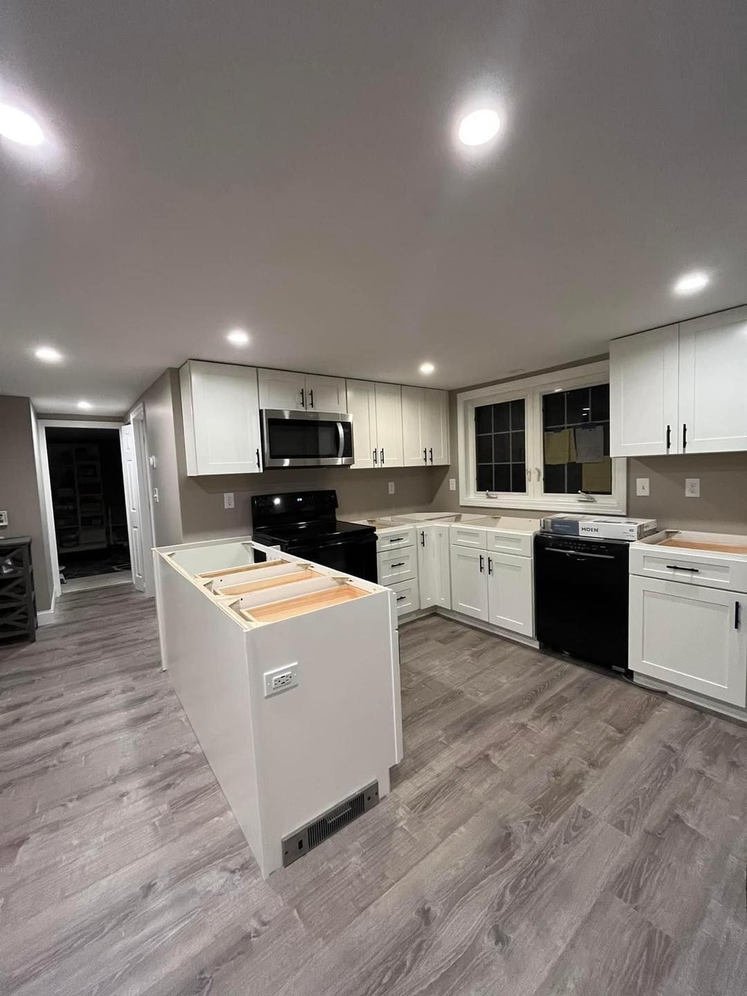 A kitchen with white cabinets, black appliances and a large island