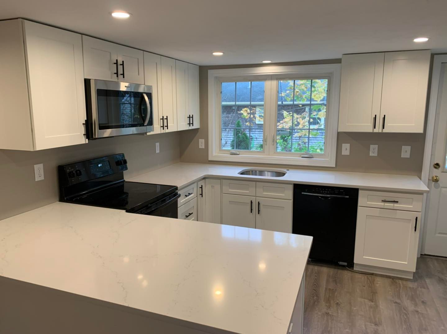 A kitchen with white cabinets, black appliances and a large window