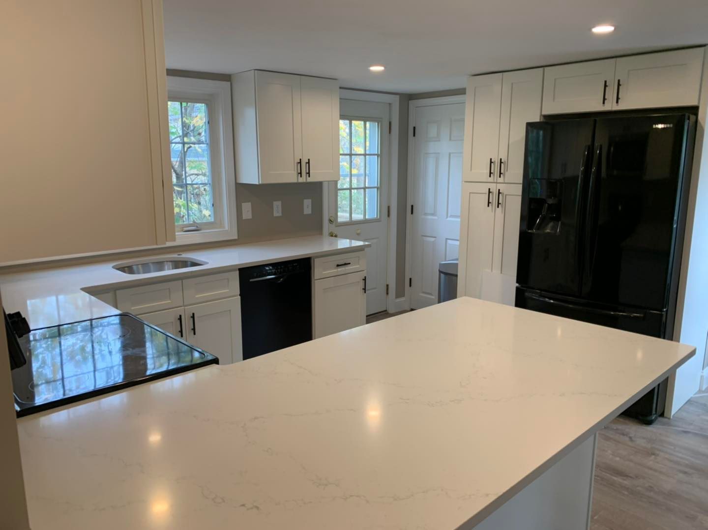 A kitchen with white cabinets, black appliances and a large island