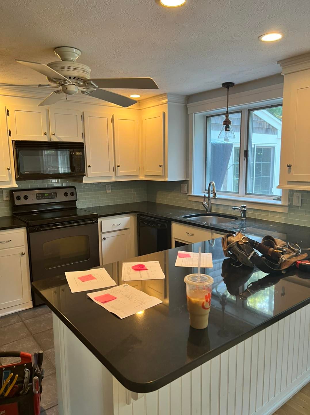 A kitchen with white cabinets and black counter tops and a ceiling fan