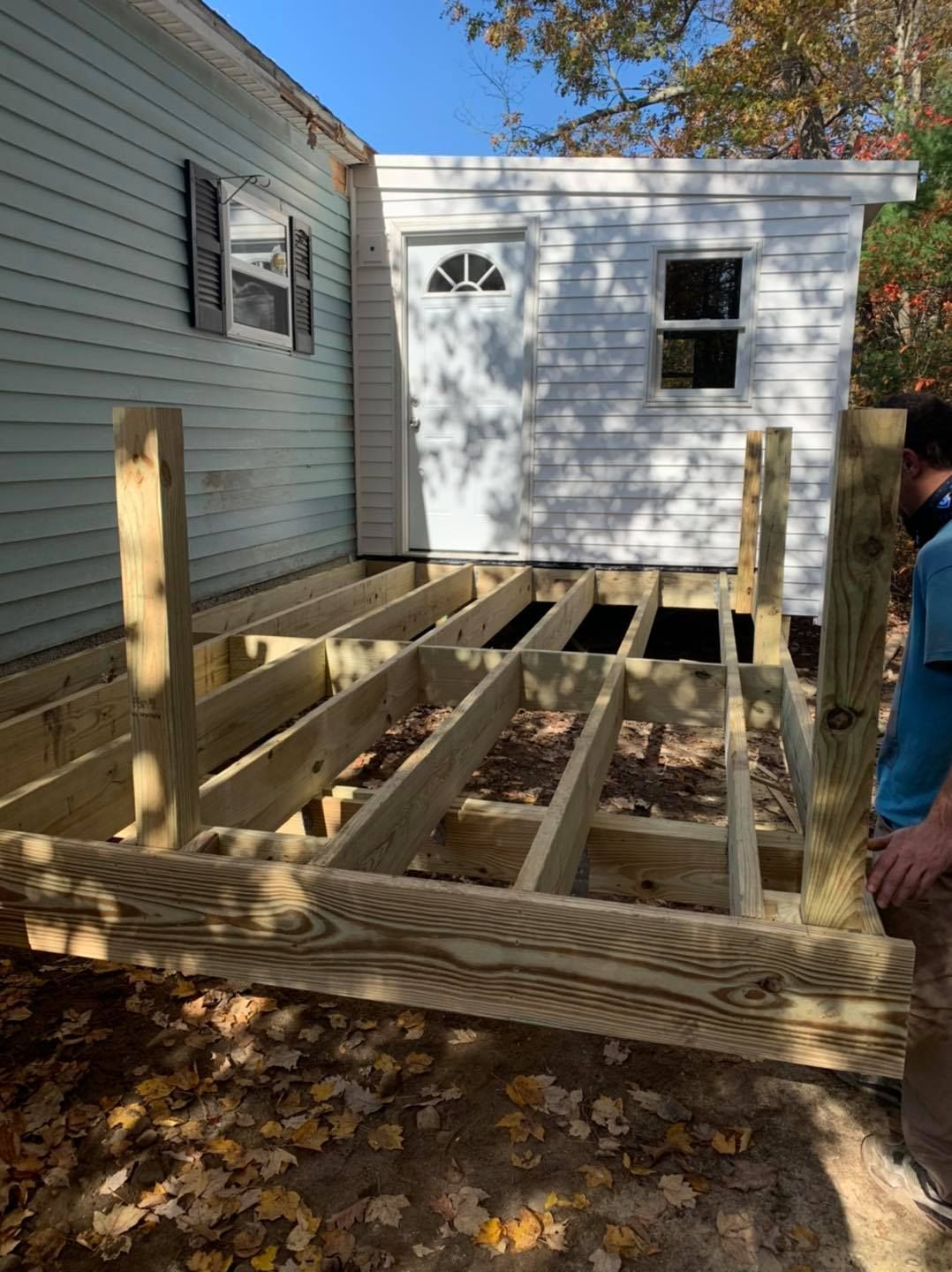 A man is standing next to a wooden deck under construction in front of a white house
