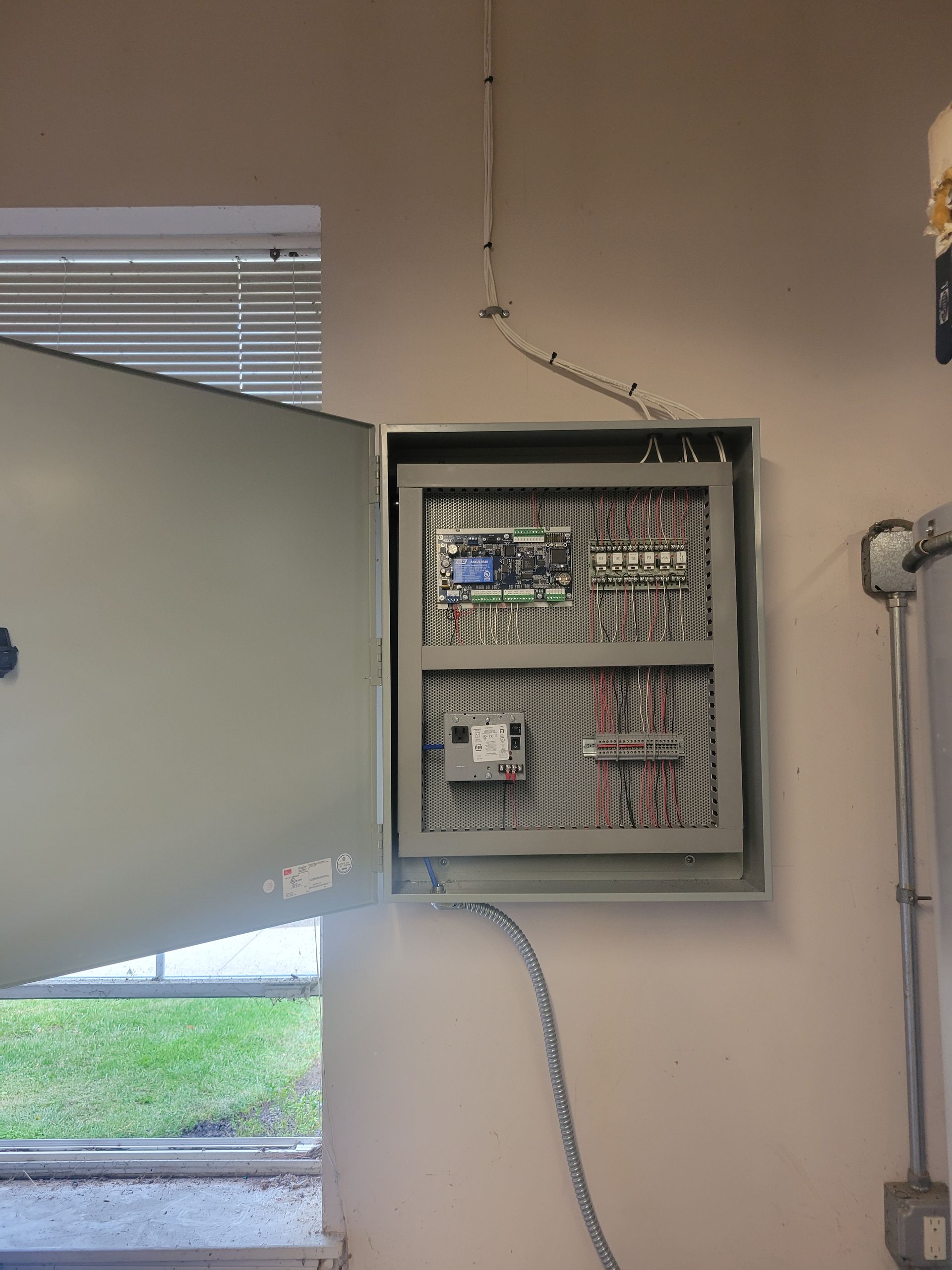 A electrical box is hanging on a wall next to a window.