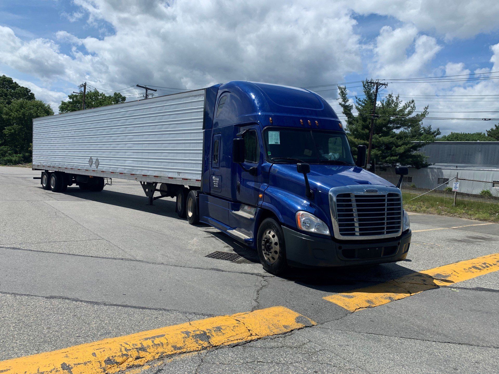 Blue semi-truck with silver trailer parked on a road under a cloudy sky