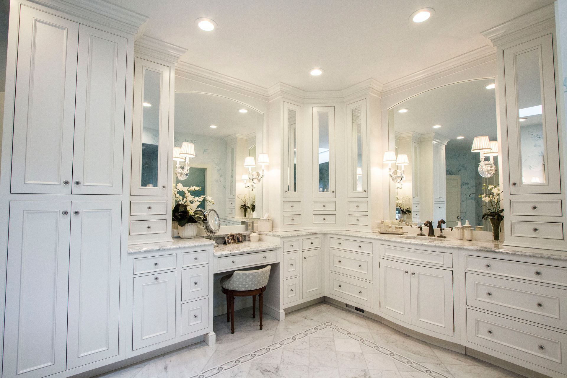 Bright white luxury bathroom with vanity, mirrors, cabinets, and marble flooring.