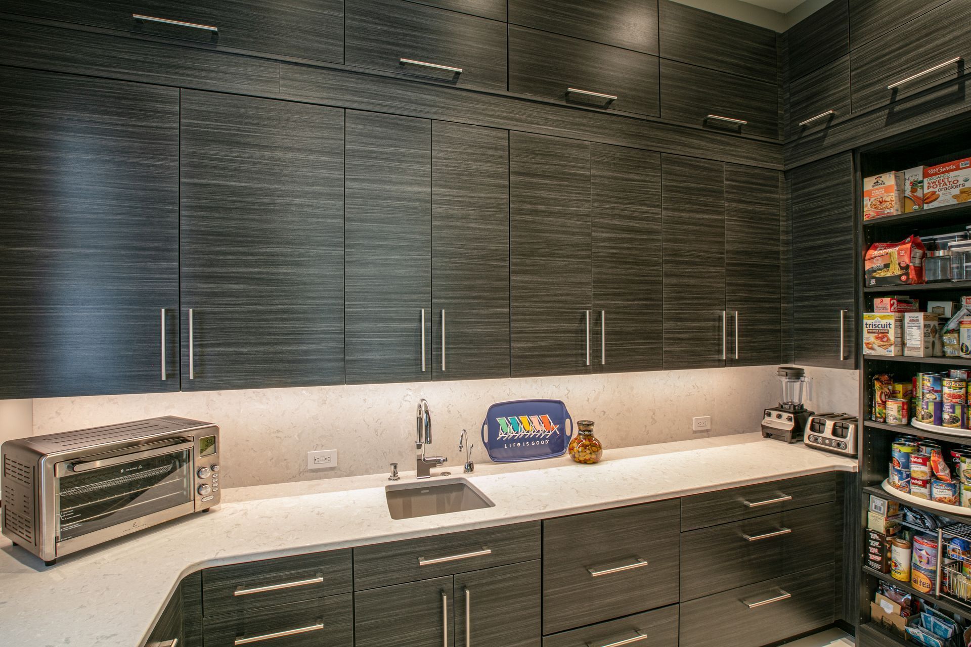 Dark gray kitchen with white countertop, cabinets, sink, toaster oven, and pantry.