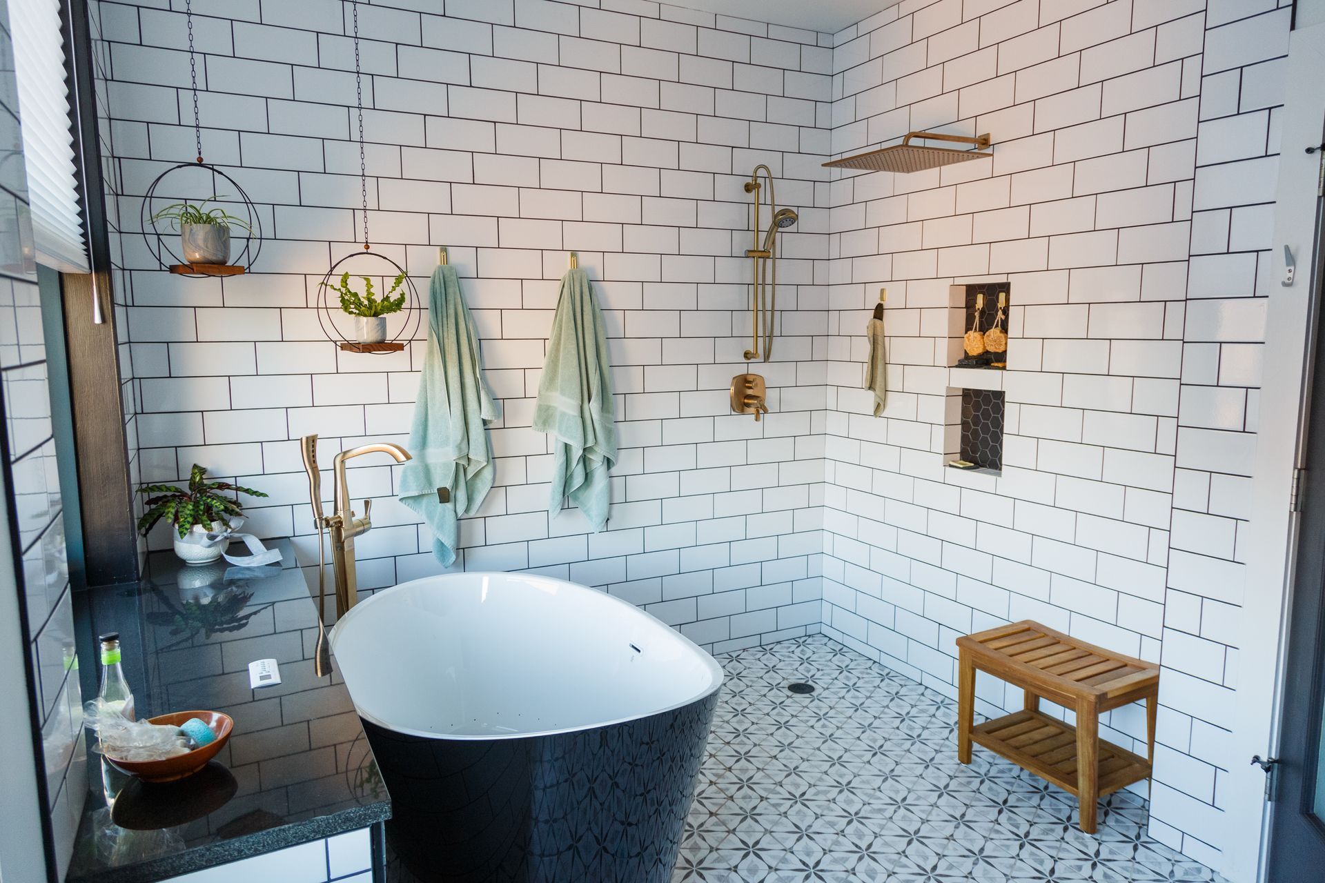 Modern bathroom with black bathtub, white brick-like tile walls, shower, and wooden bench.