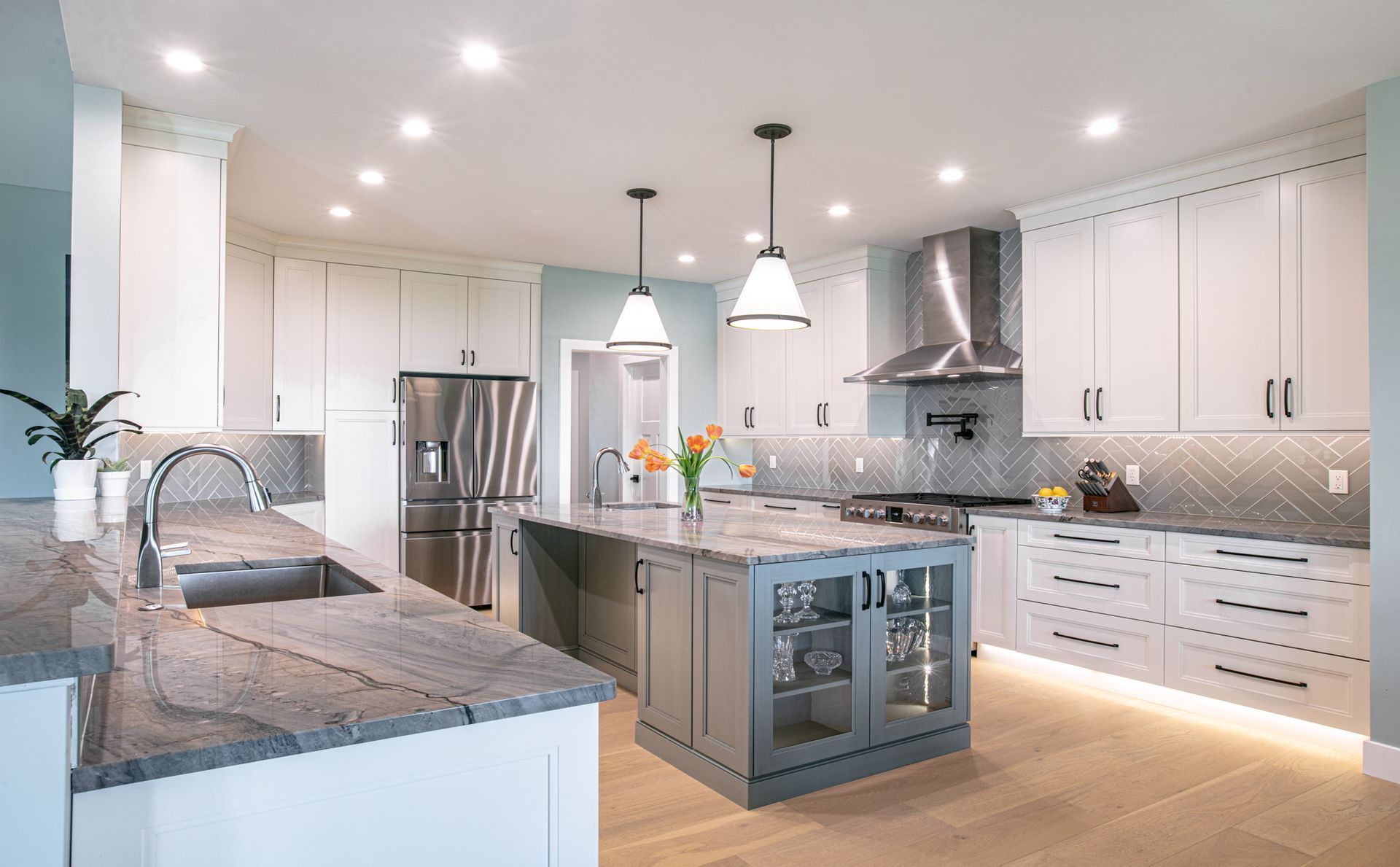 Modern kitchen with white cabinets, gray countertops, stainless steel appliances, and a blue island.