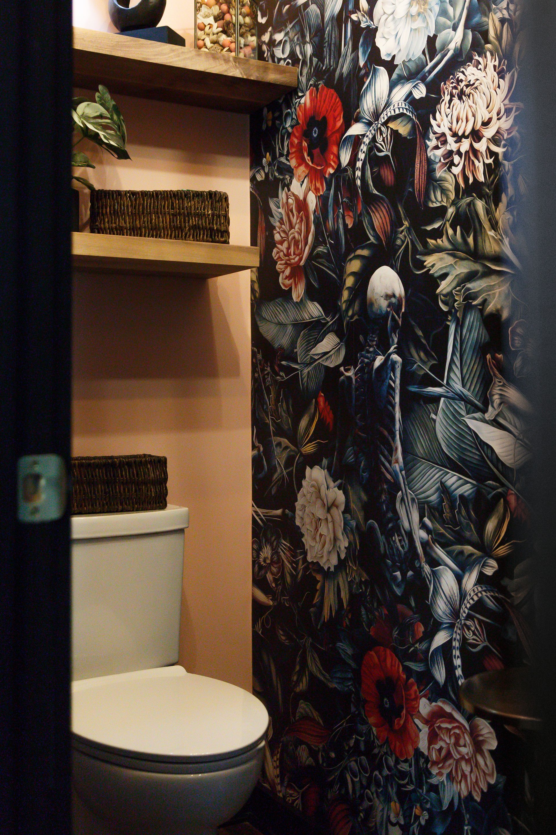 Small bathroom with floral wallpaper, pink walls, and wooden shelves. A toilet is visible.