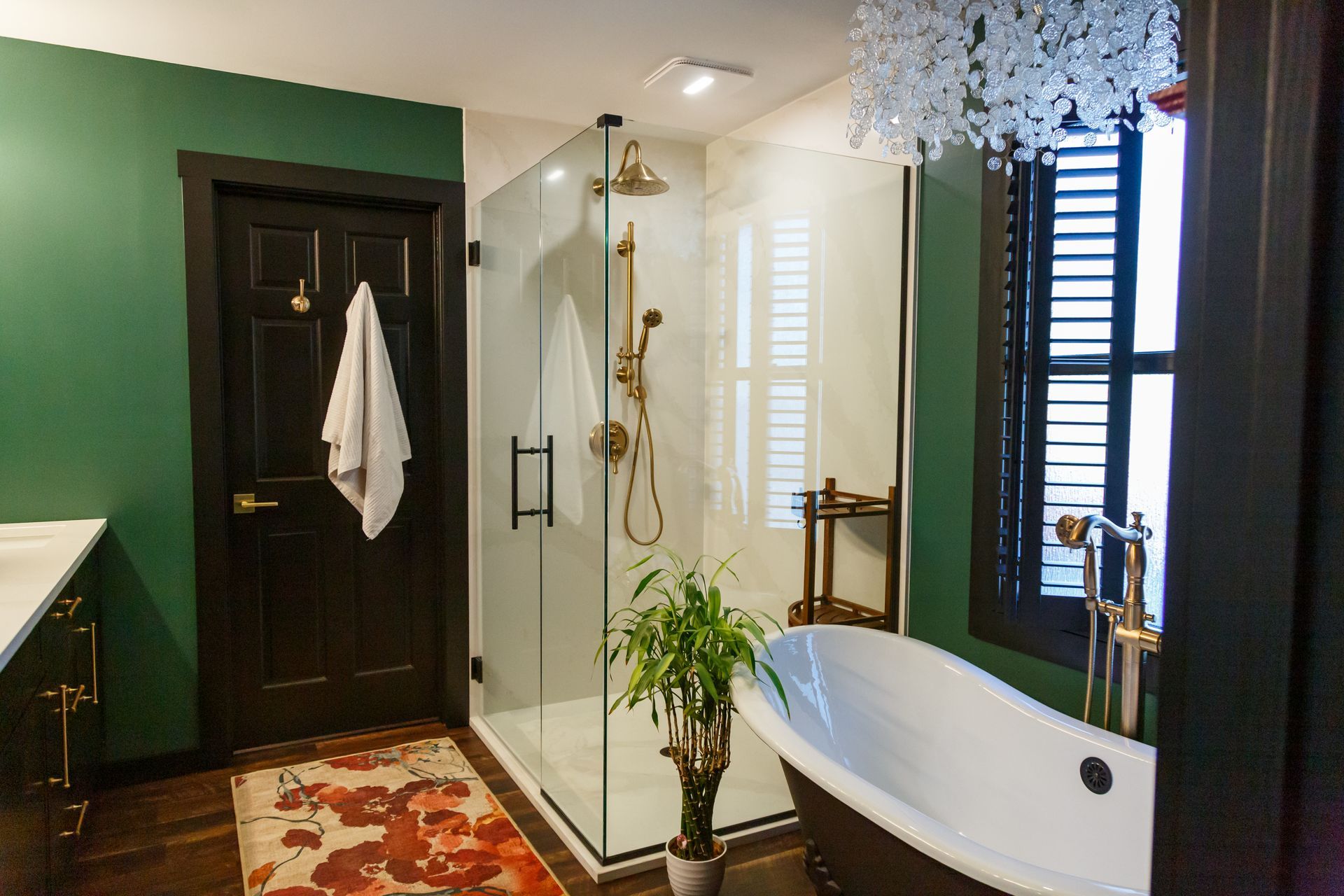 Green bathroom with glass shower, freestanding tub, dark wood trim, and floral rug.