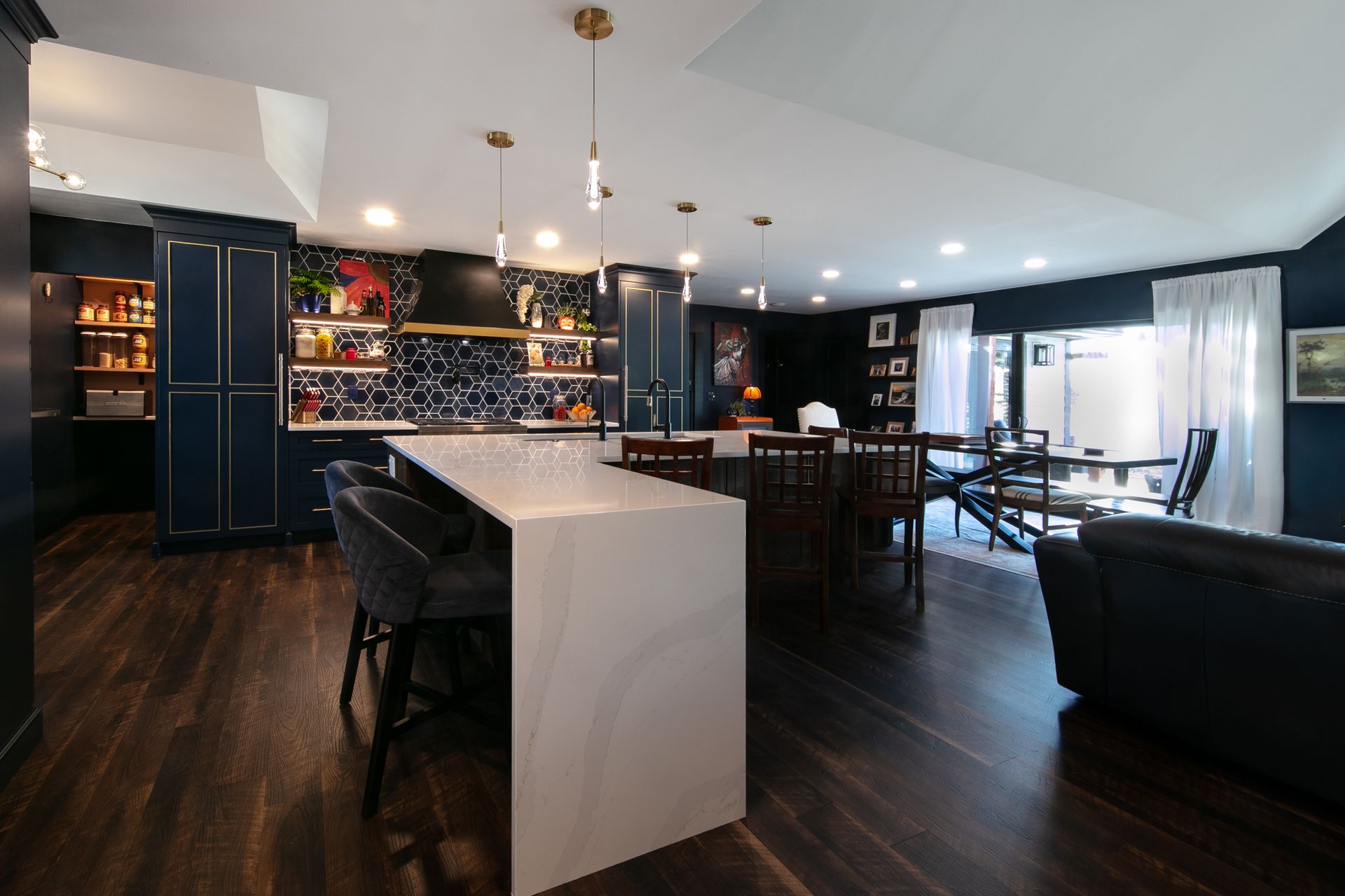 Open-concept kitchen with navy cabinets, white island, and dining area with dark wood flooring.
