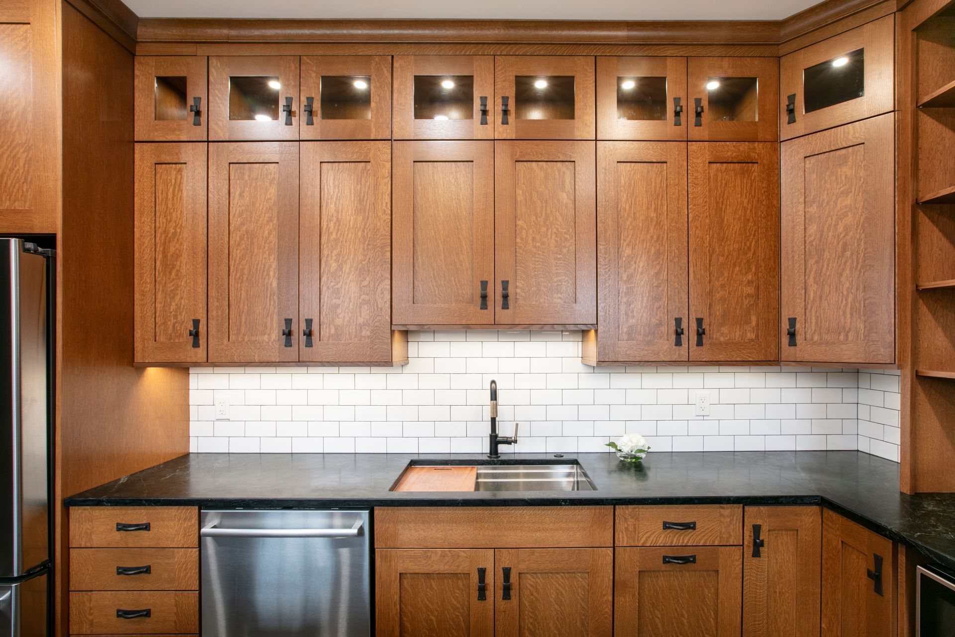 Kitchen with wooden cabinets, black countertops, stainless steel appliances, and white subway tile backsplash.