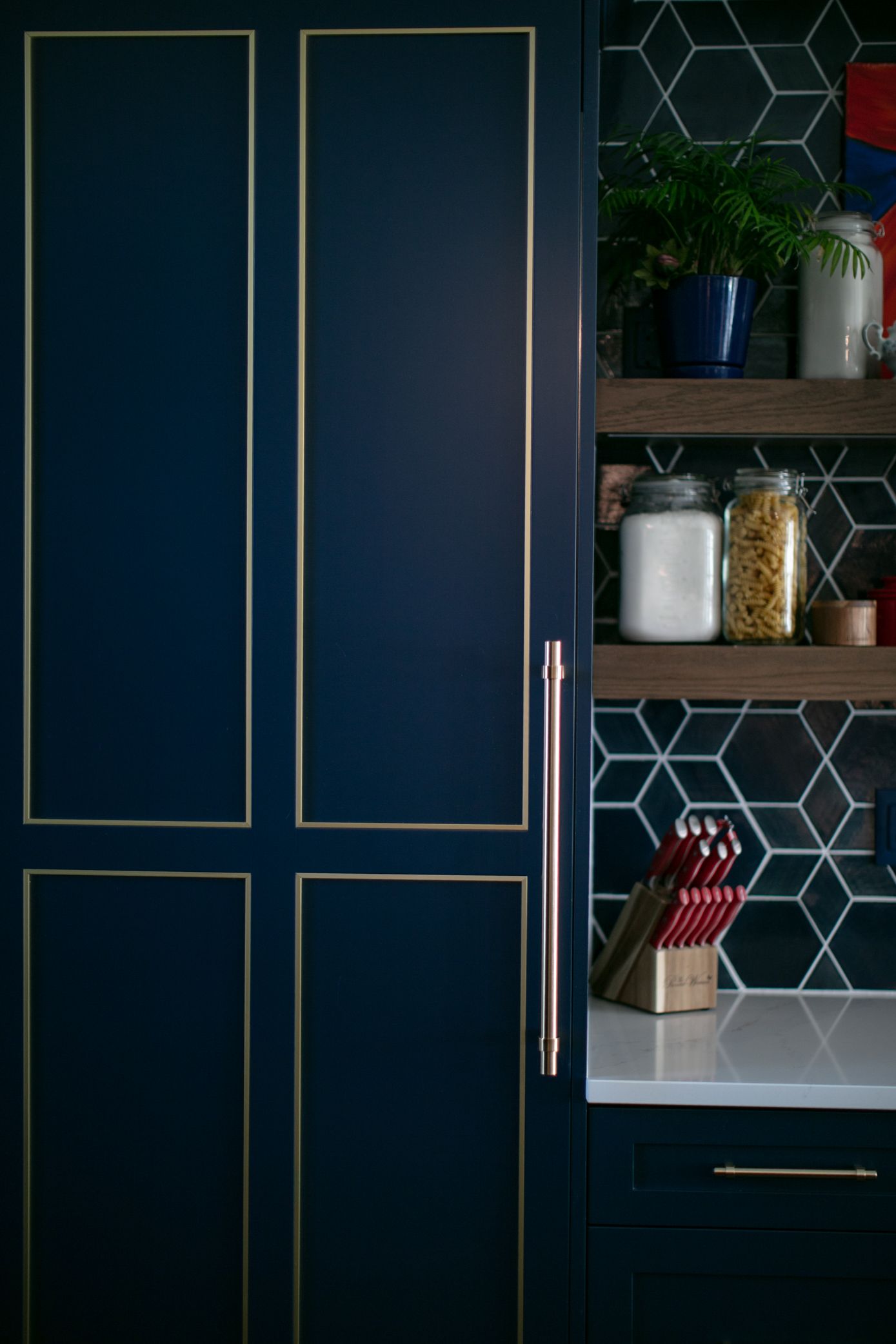 Dark blue kitchen cabinet with gold trim; adjacent open shelves with items.