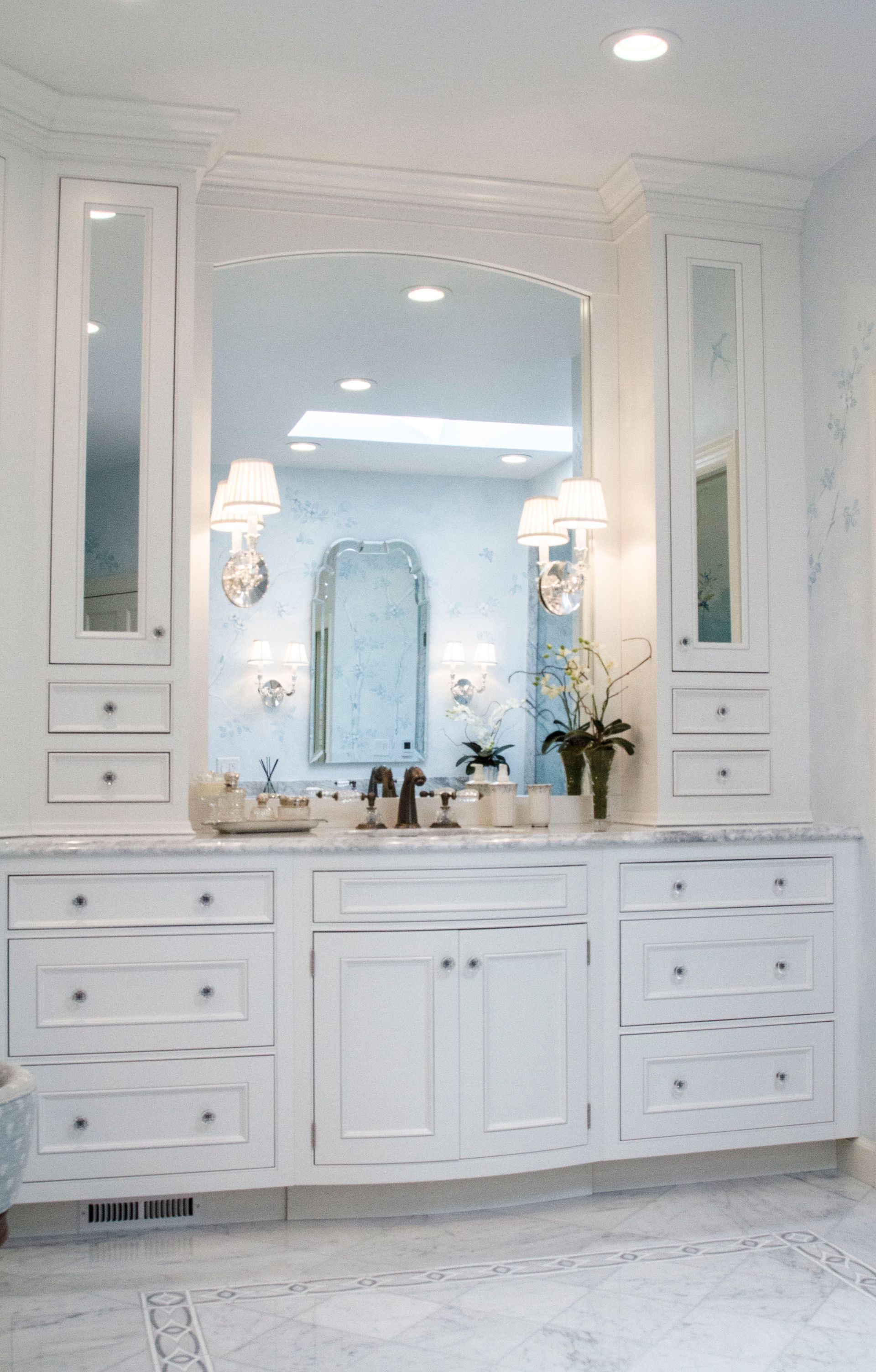 White bathroom vanity with marble countertop and ornate mirrors.
