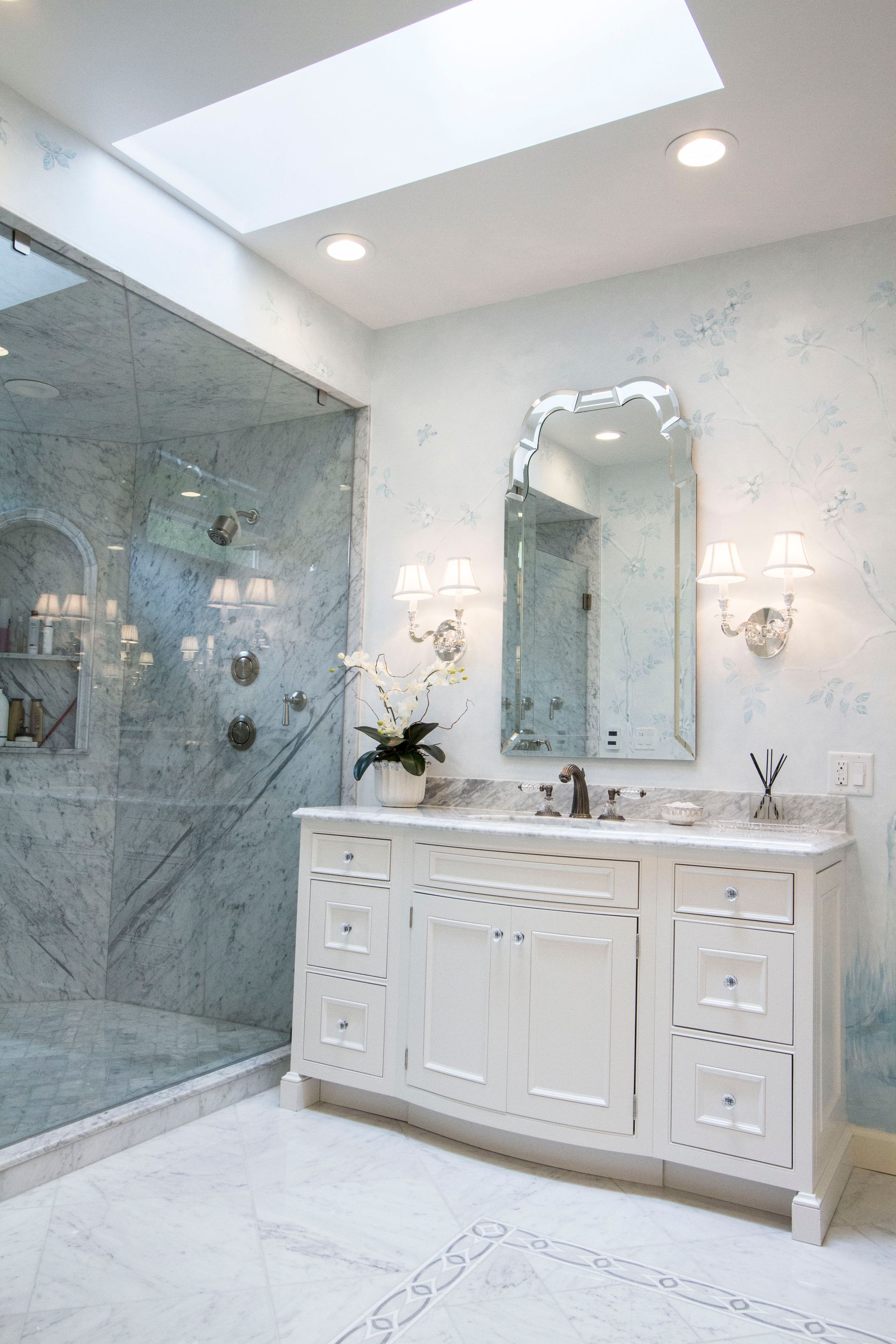 Luxurious white marble bathroom with a large vanity, shower, and skylight.