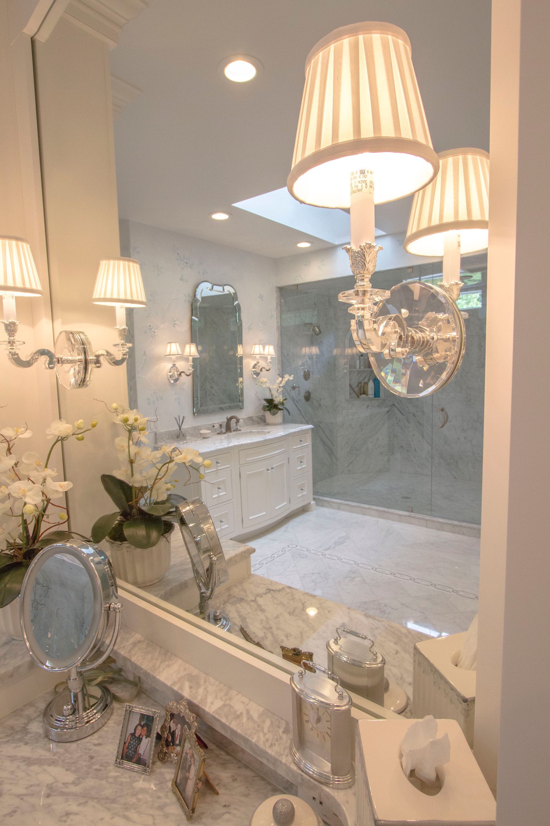 Elegant bathroom with marble countertop, mirror, sconces, and shower.