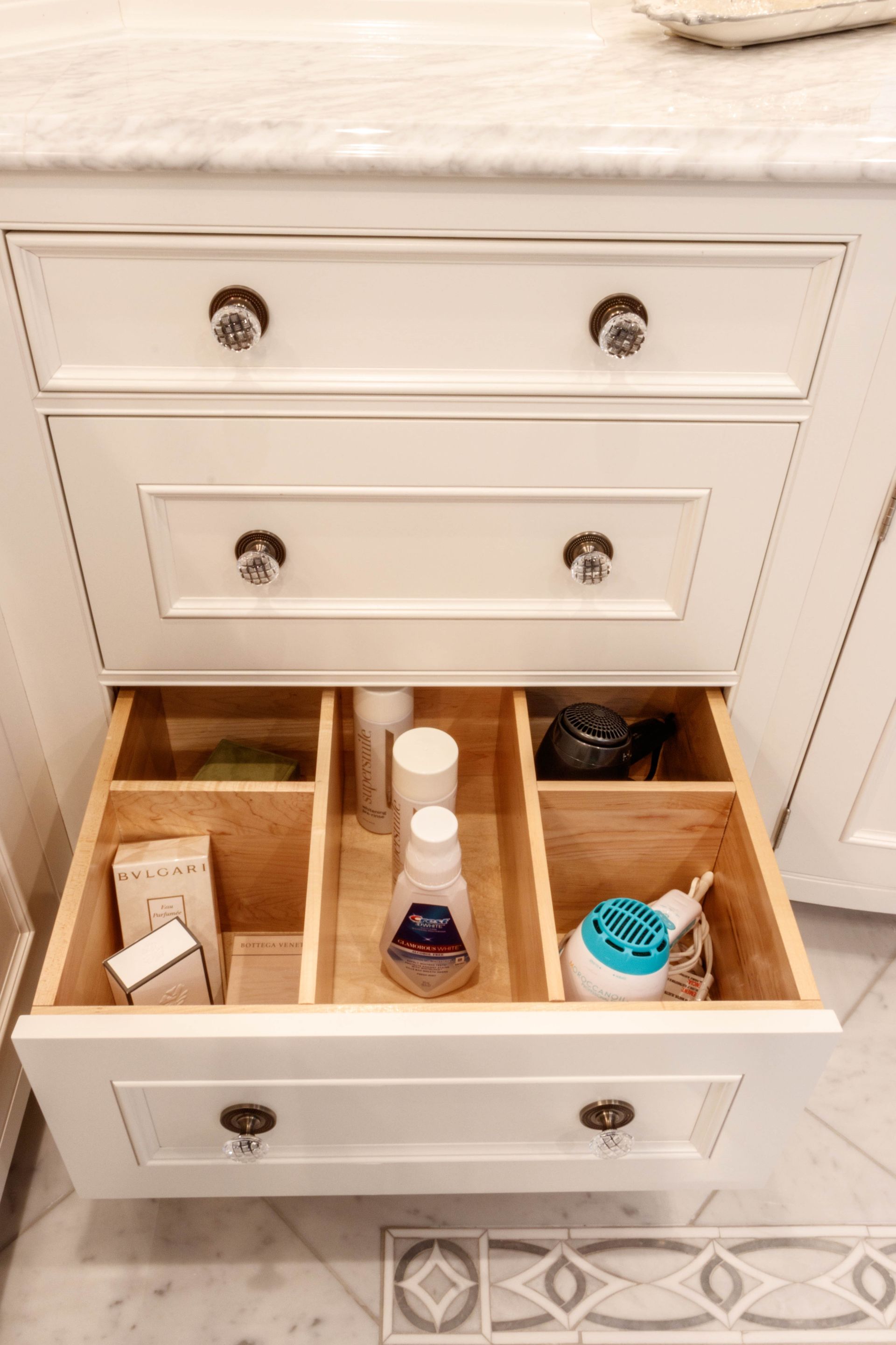 White bathroom vanity with open drawer, containing toiletries organized in wooden dividers.