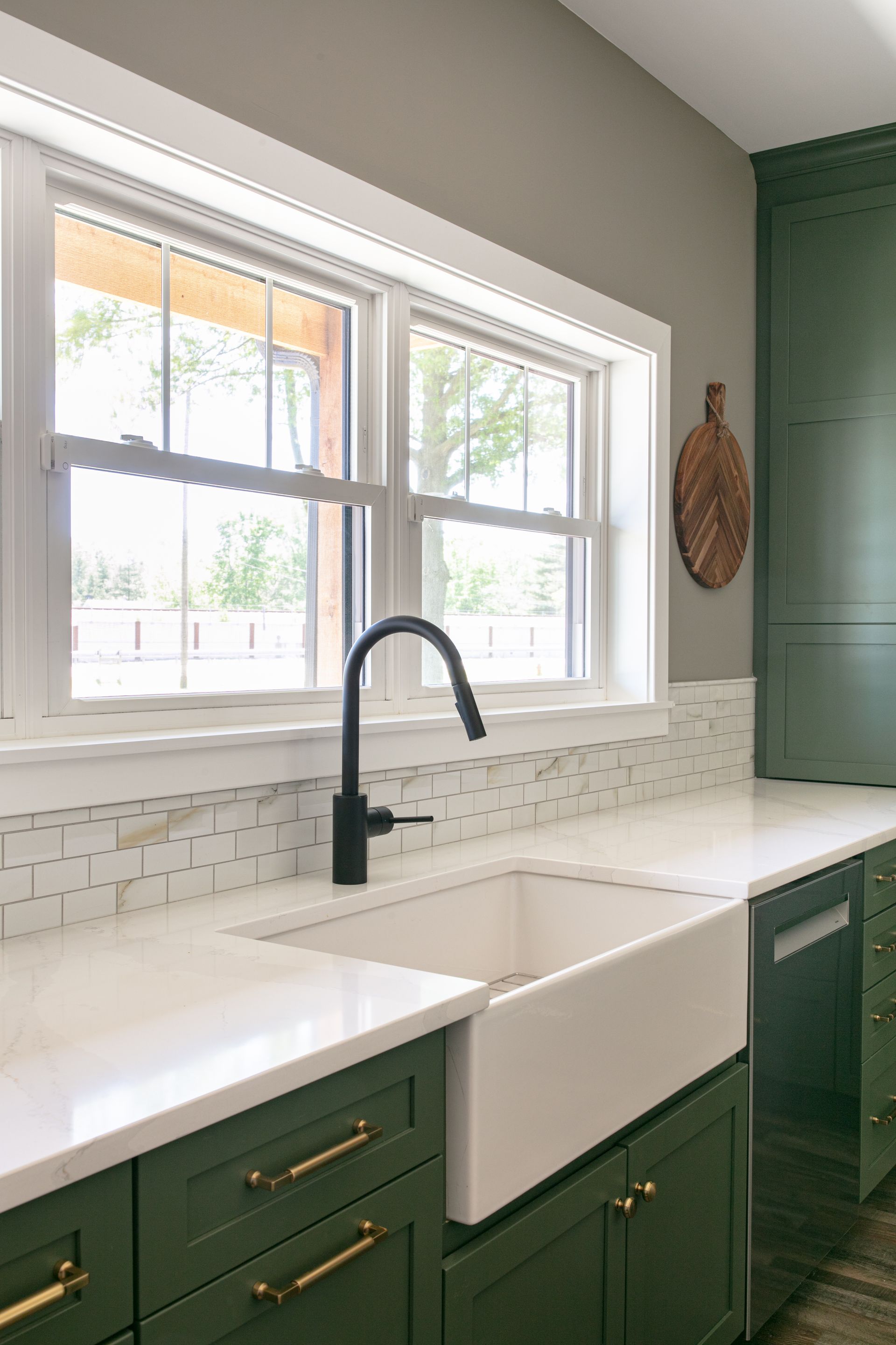 Green kitchen with white countertops, apron-front sink, black faucet, and two windows.