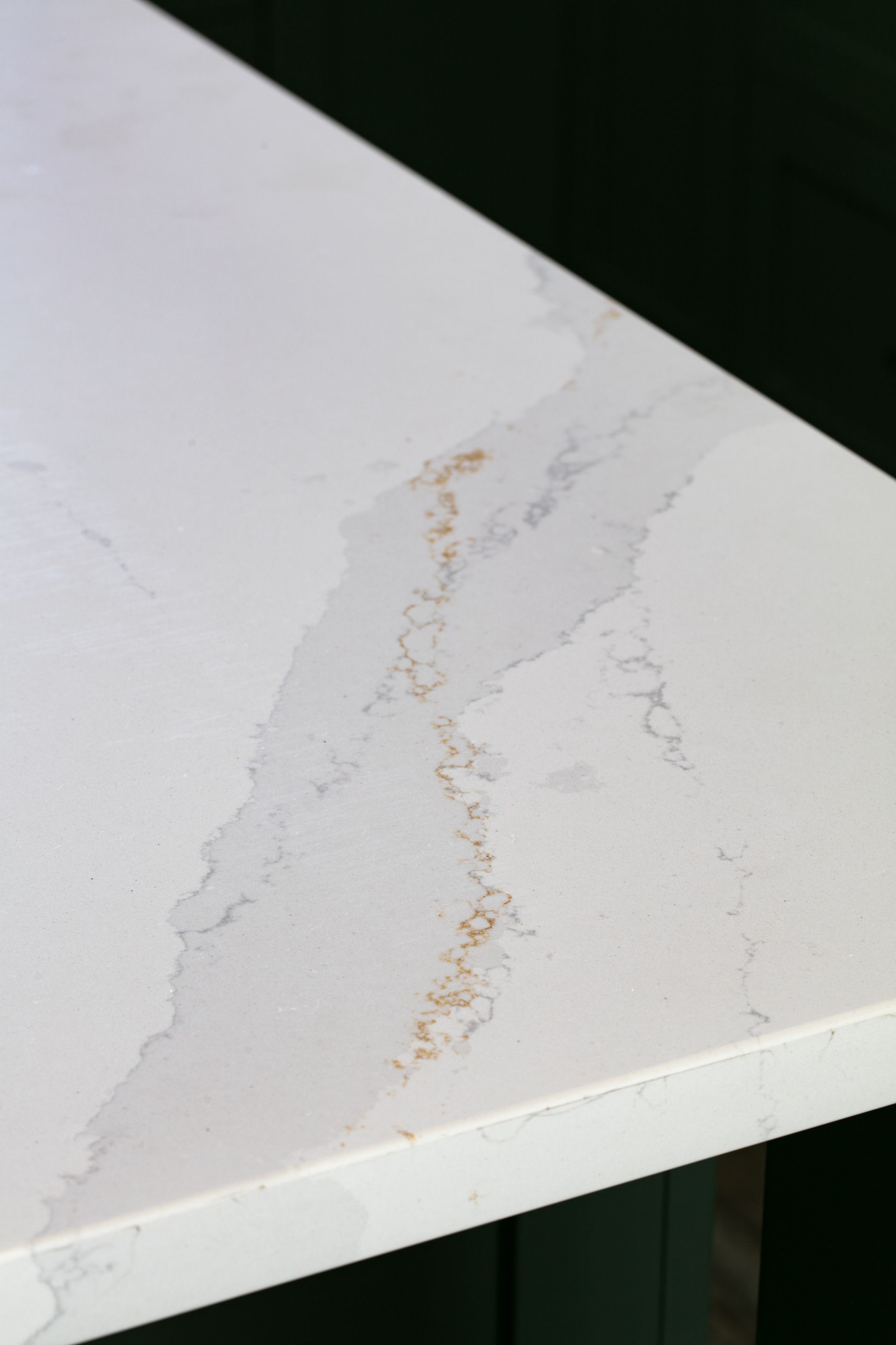 Close-up of a white countertop with grey veining and gold accents. Dark green background.