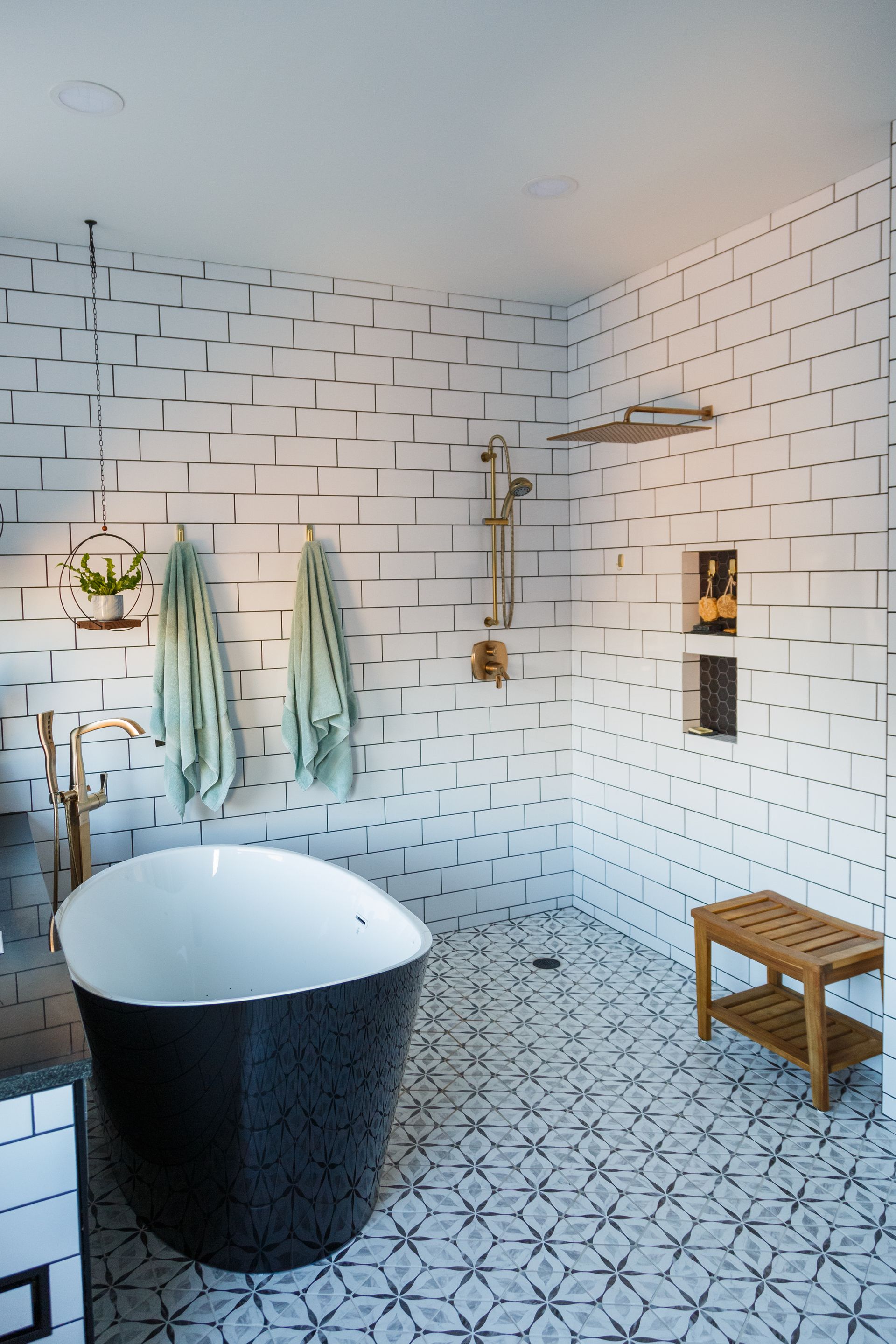 Bathroom with black and white tile, a black tub, and a shower with a wooden bench.