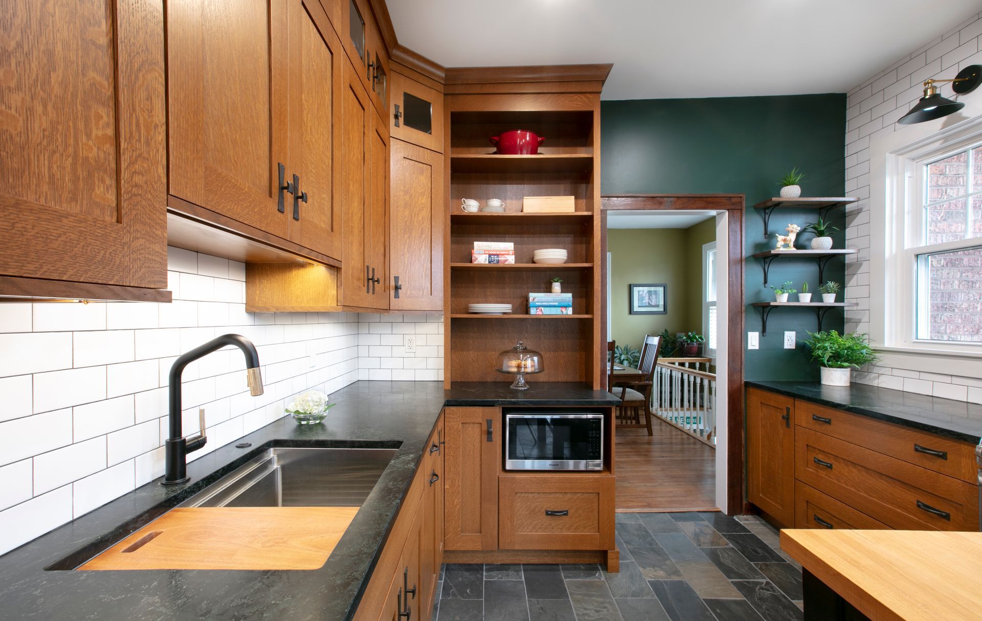 Kitchen with wood cabinets, black countertops, stainless steel sink, subway tile backsplash.