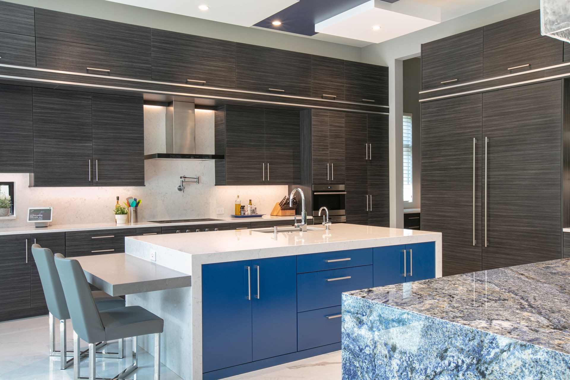 Modern kitchen with dark gray cabinets, blue island, white countertops, stainless steel appliances.