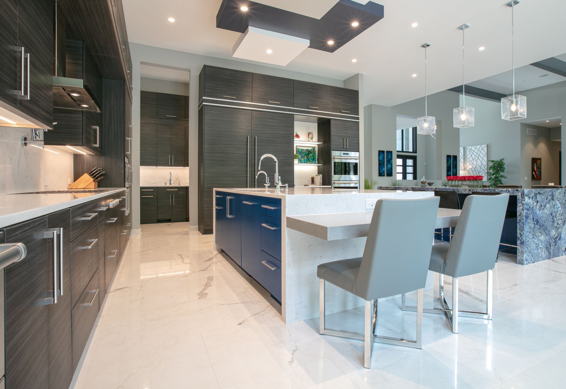 Modern kitchen with dark cabinetry, blue island, marble floors, and light fixtures.