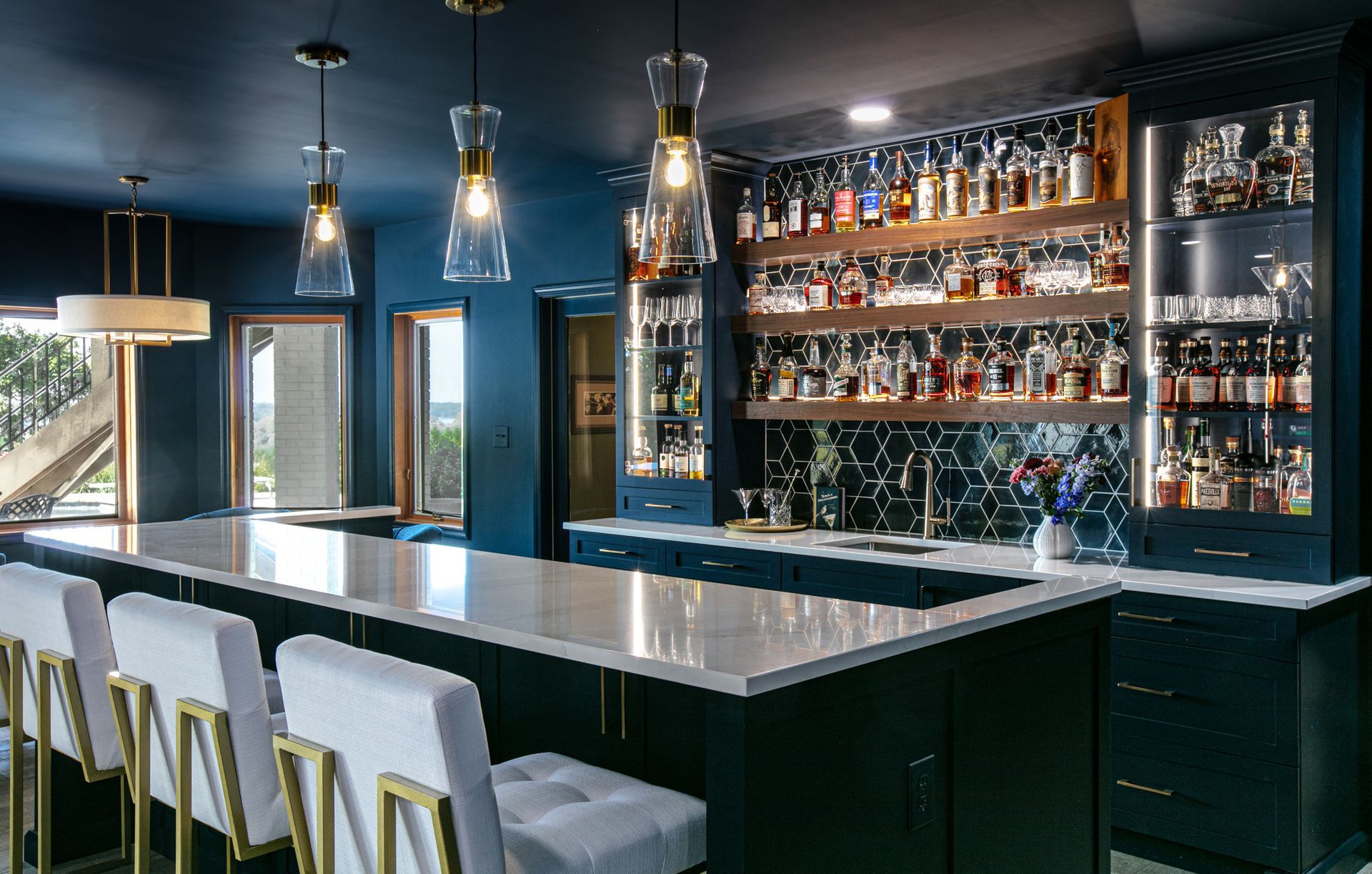 Luxurious dark blue bar with a marble countertop, seating, and liquor display.