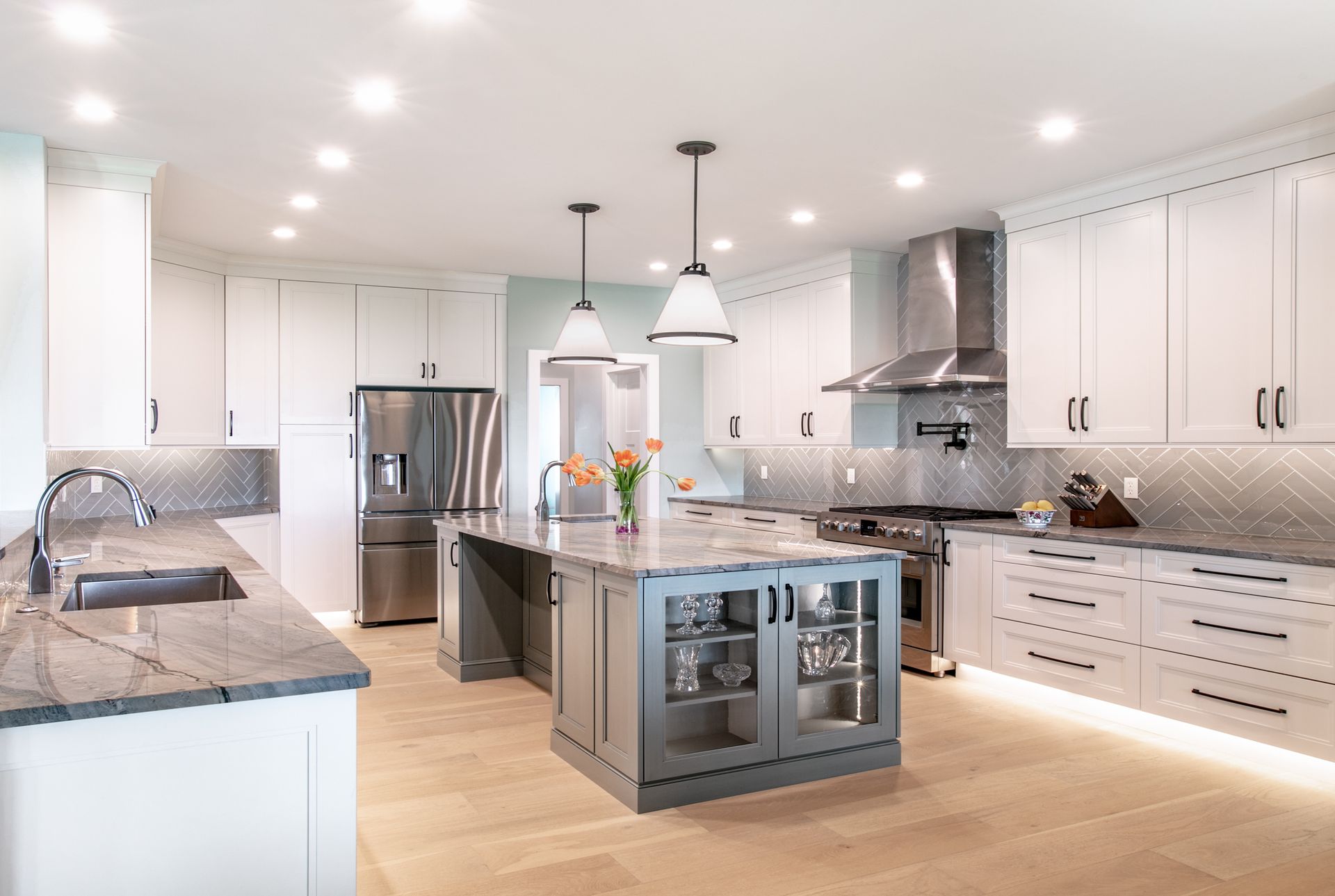 Modern white kitchen with gray island and countertops, stainless steel appliances, and wood flooring.