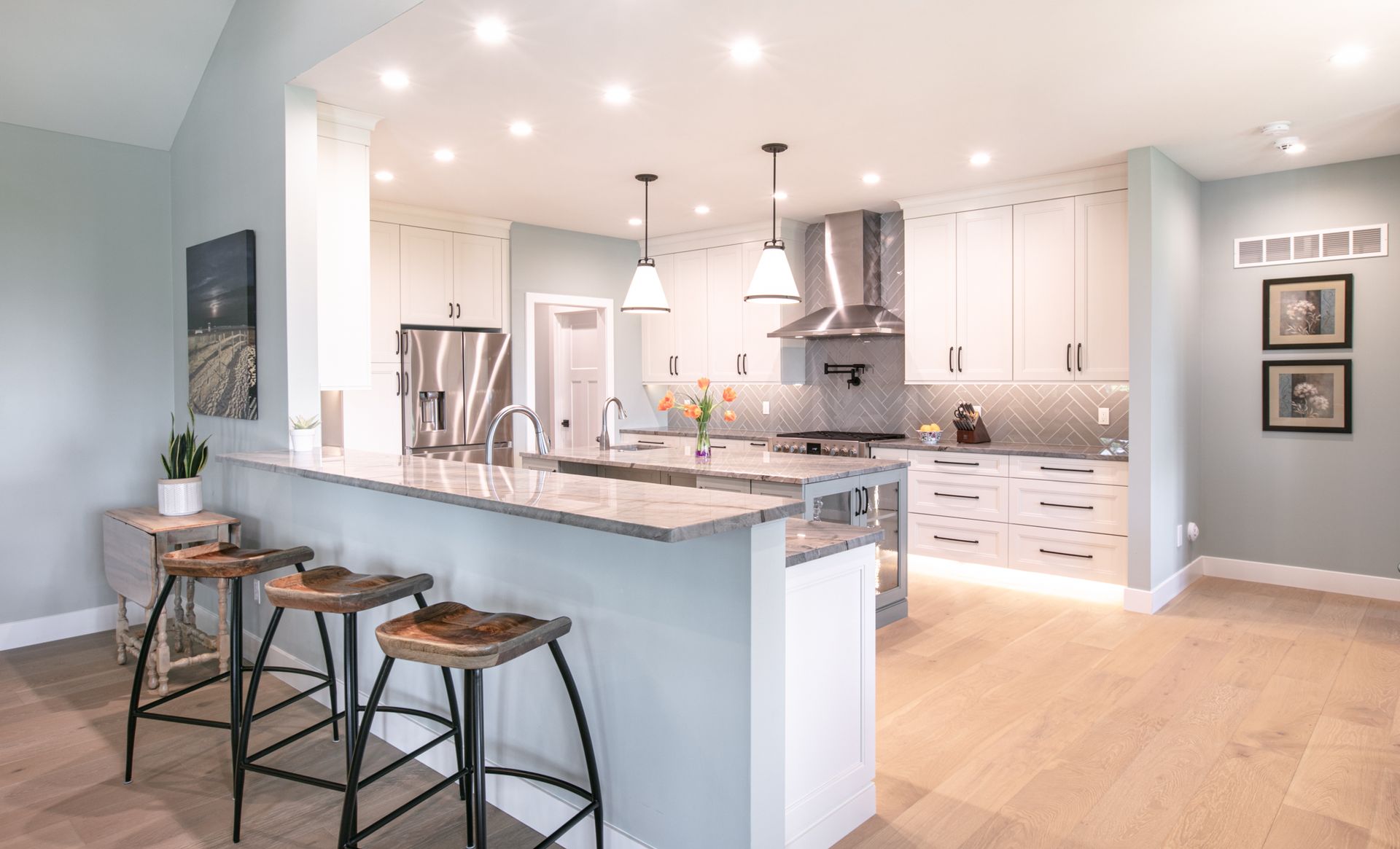 Modern kitchen with white cabinets, marble countertops, breakfast bar with stools, and pendant lights.