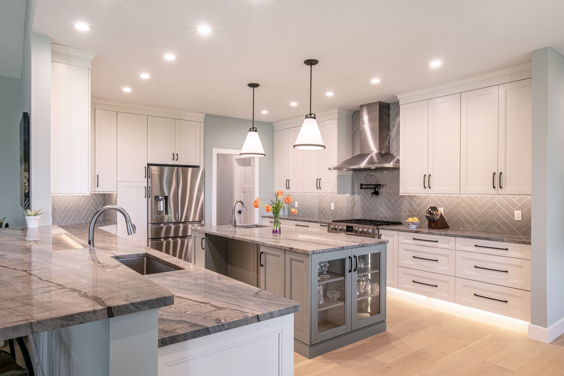 Modern kitchen with gray and white cabinets, stainless steel appliances, and a light blue backsplash.
