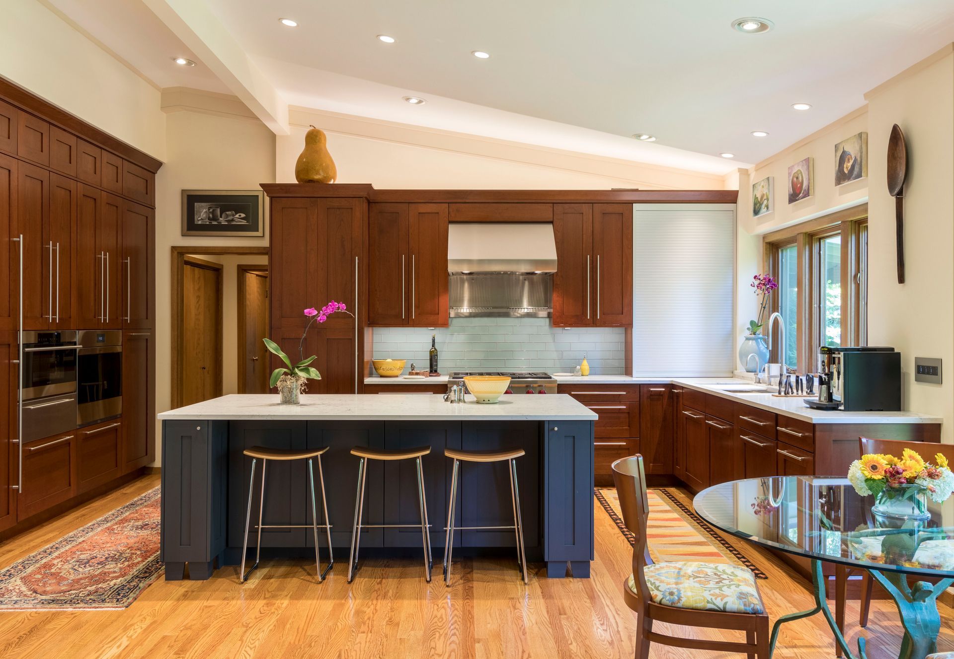 Spacious kitchen with dark wood cabinets, a navy island with stools, and a glass-top table.