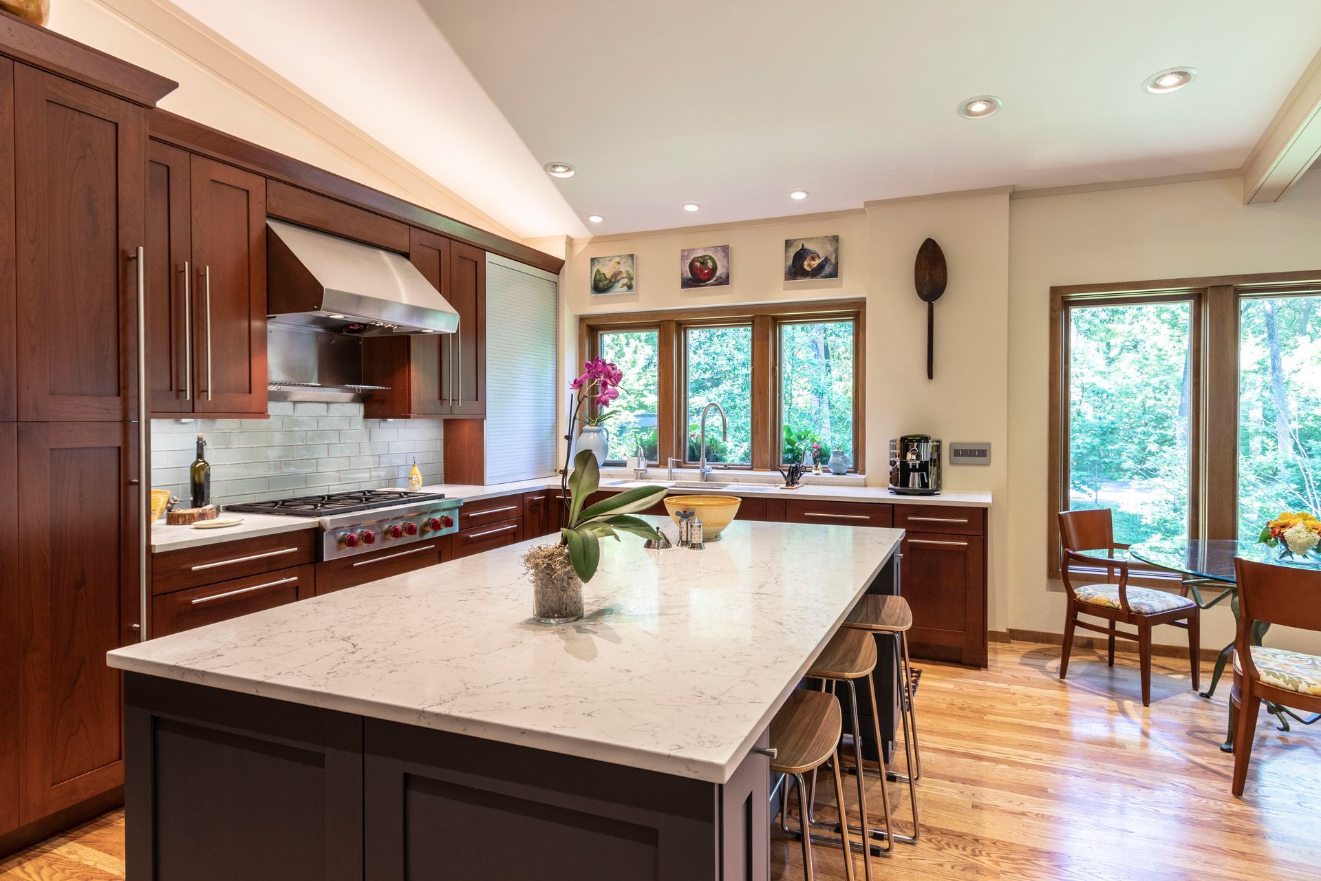 Kitchen with dark wood cabinets, large island with seating, and a view of trees through the windows.
