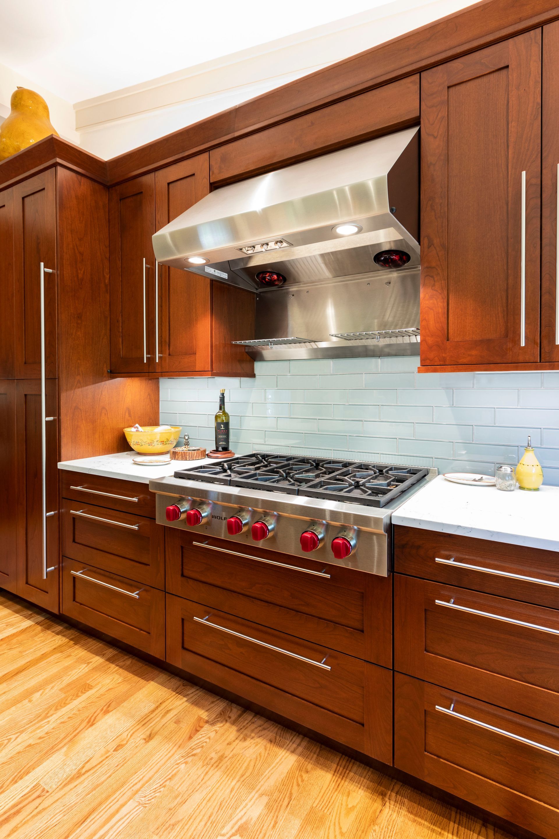 Kitchen with cherry wood cabinets, stainless steel stove and hood, white countertop, and light wood floor.