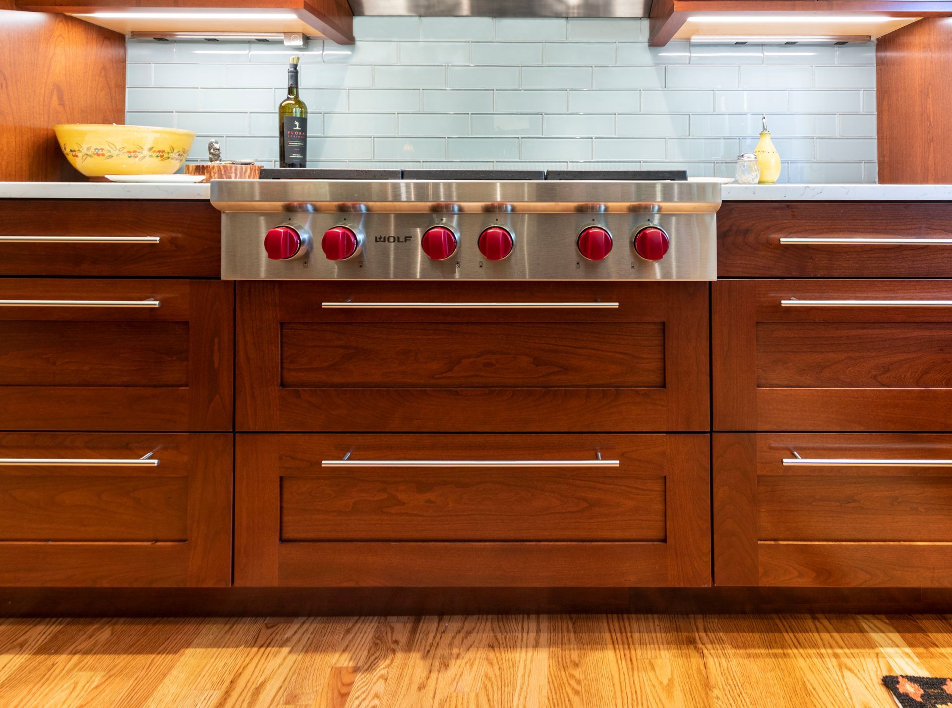 Kitchen with a stainless steel range and red knobs, wooden cabinets, and light blue backsplash.