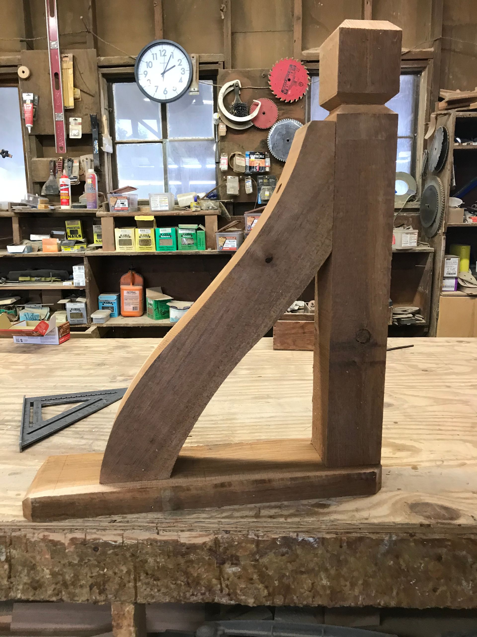 Wooden bracket in a workshop. The brown bracket is sitting on a wooden table with tools and shelves in the background.