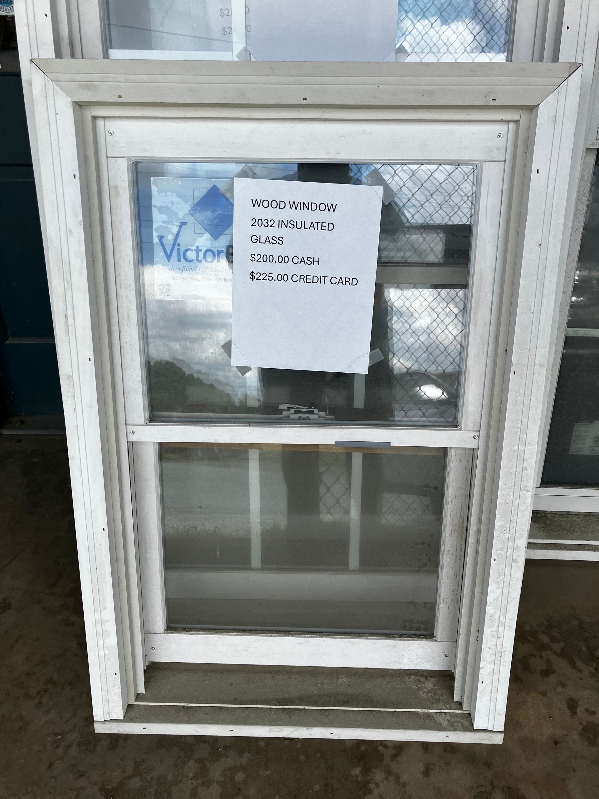 White vertical window with a paper sign taped to it. The sign has handwriting on it. The window has a grid pattern and sits outside.