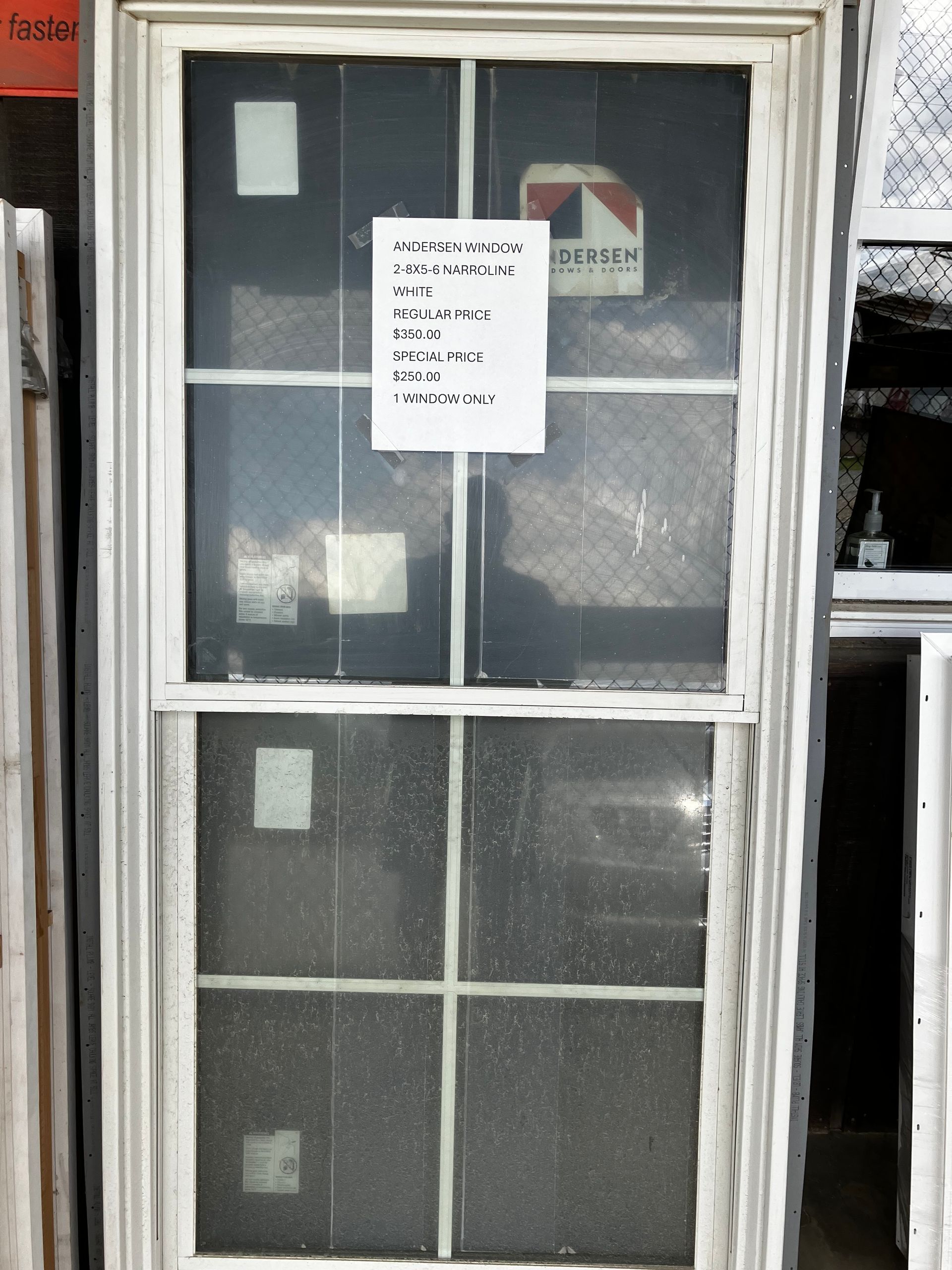 White window with a screen and a sign listing information, displayed indoors against a dark background.