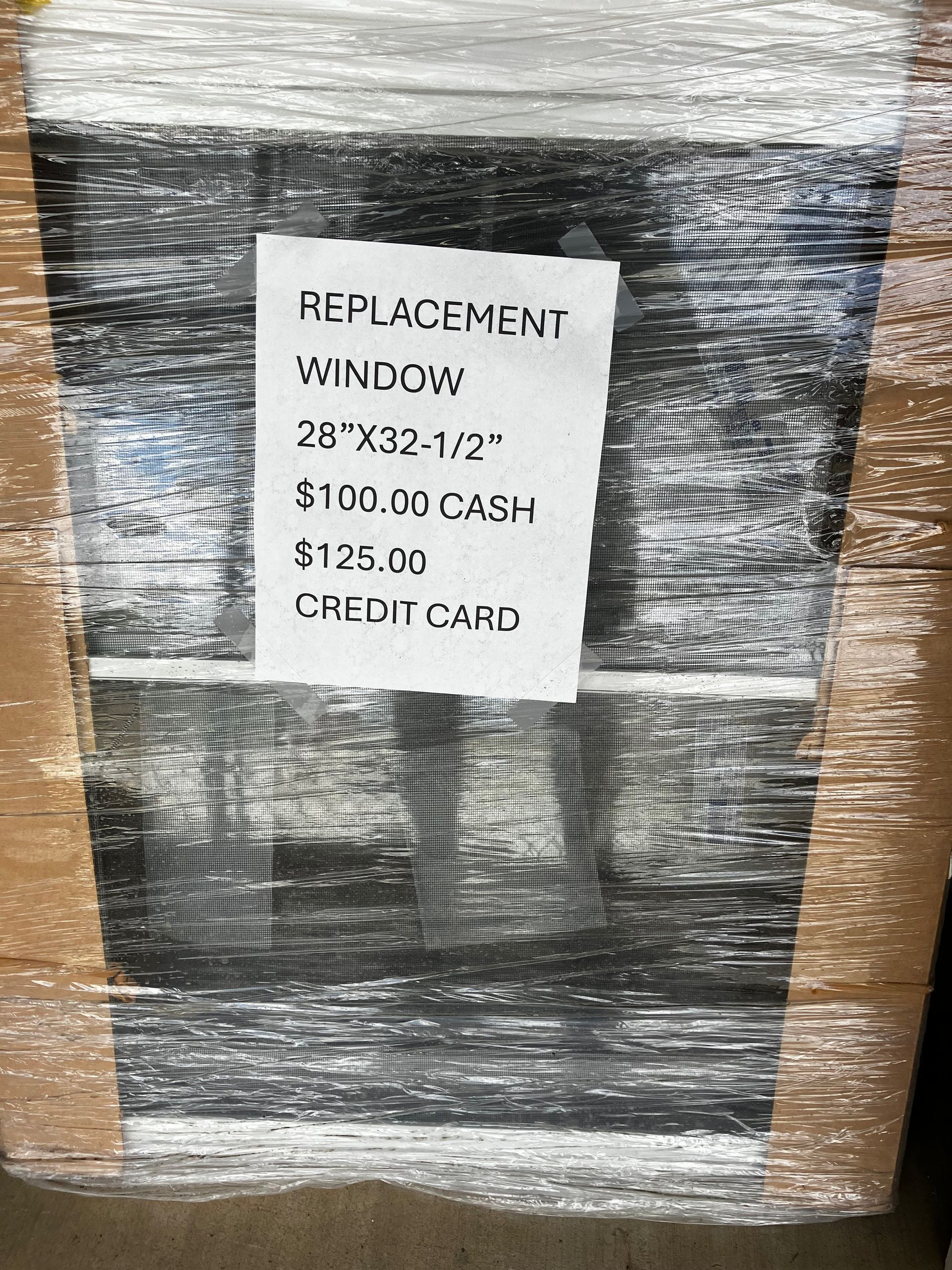 A wrapped replacement window with a handwritten sign. The sign reads