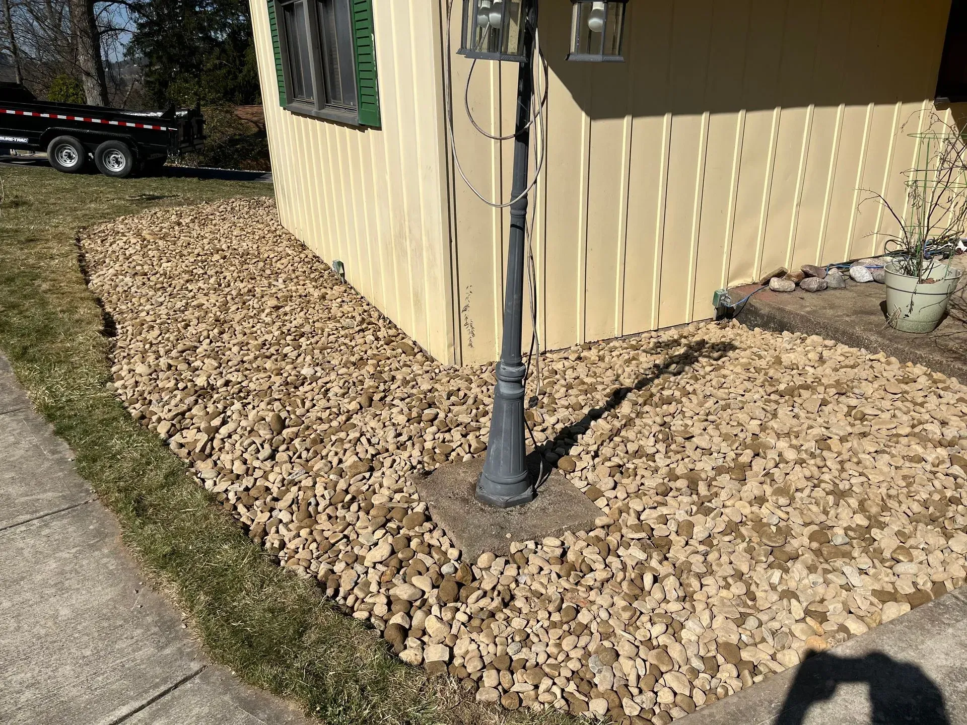 Tan rock landscaping against a yellow house, a dark lamppost, and sidewalk.