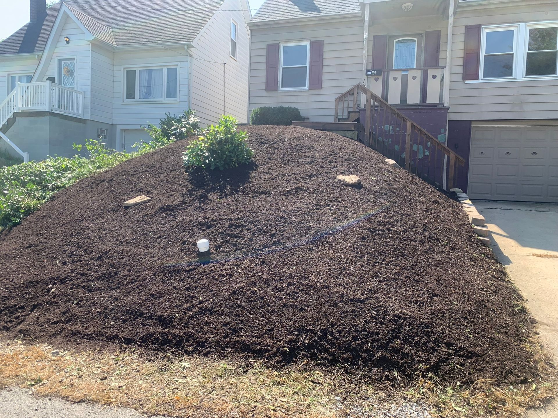 Brown mulch pile in front of a tan house and a white house.