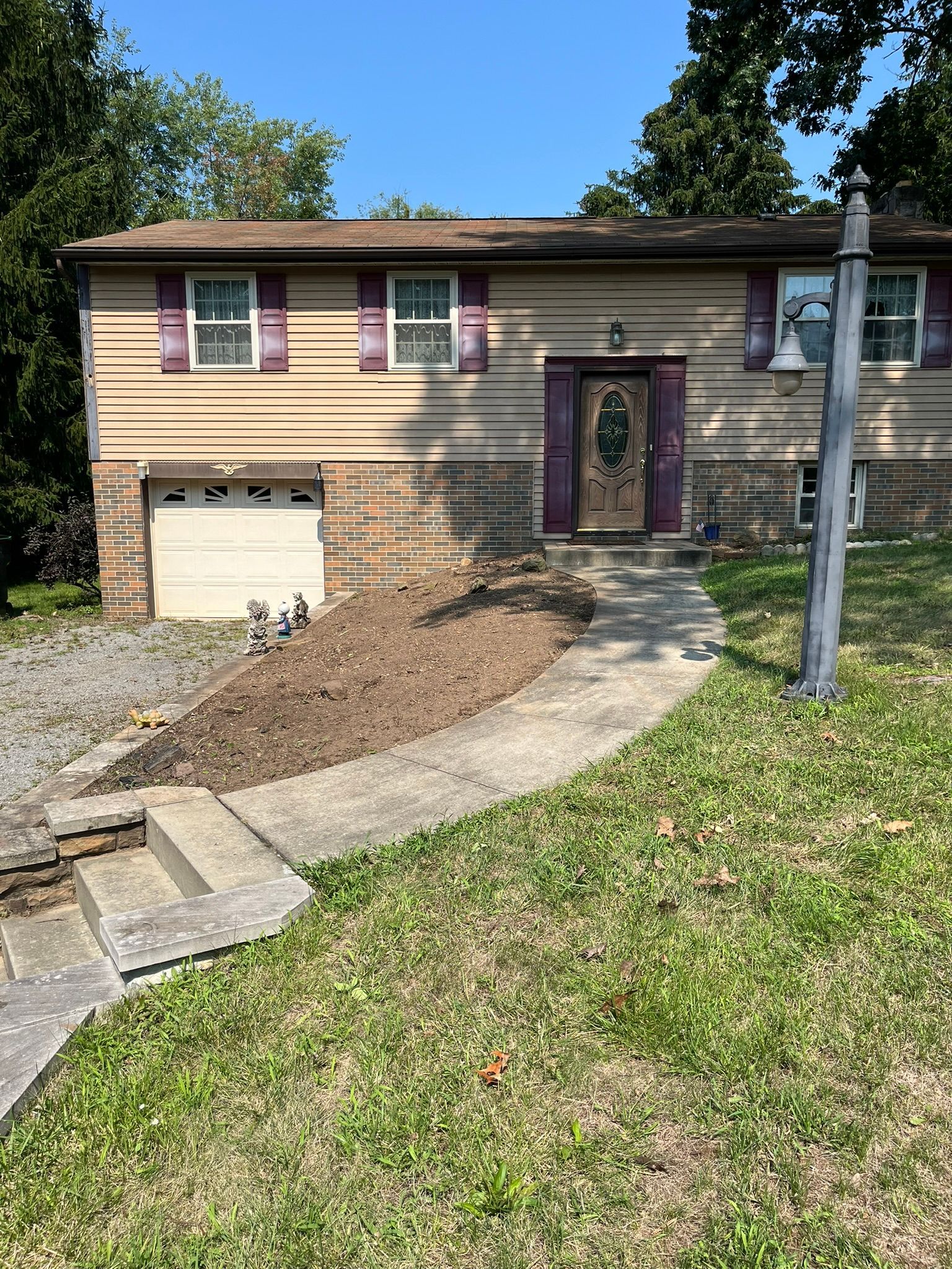 Tan house with purple shutters, concrete path, dirt patch. Garage on left, lamp post on right.