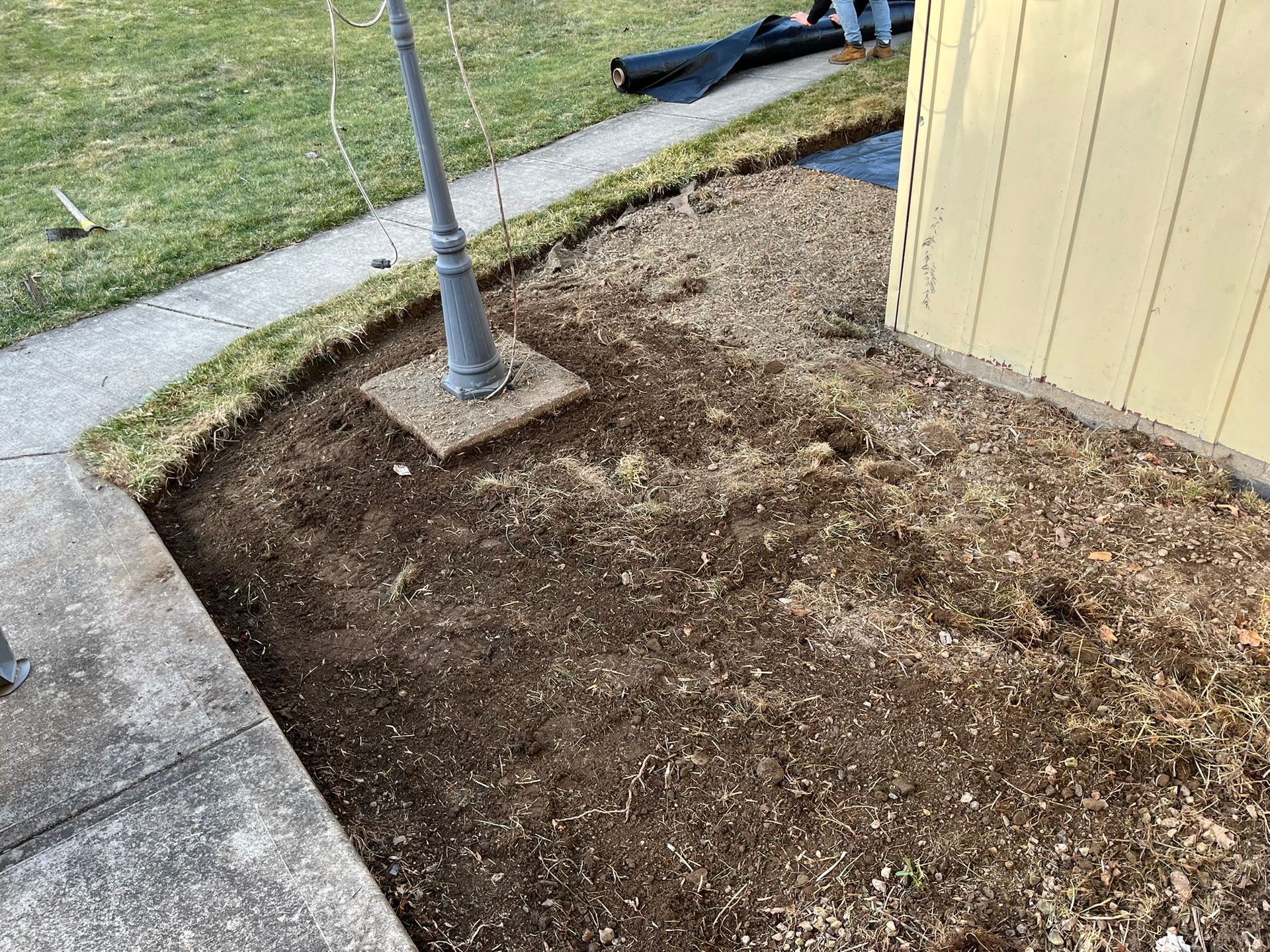 A landscaped yard with mulch, a light post, and bordering grass next to a house.