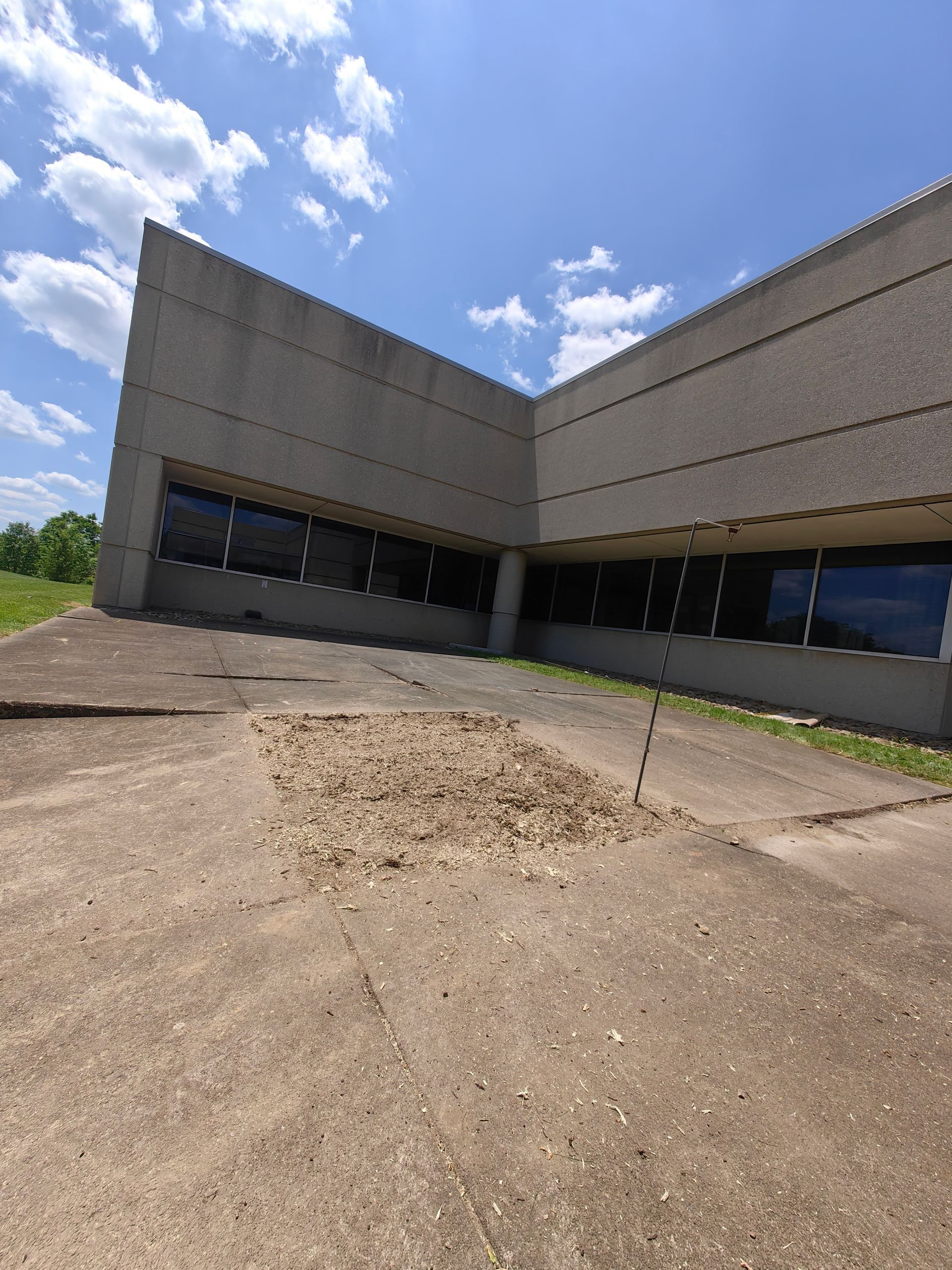 Concrete building with angled walls and windows. A patch of dirt on the concrete ground is in the foreground.